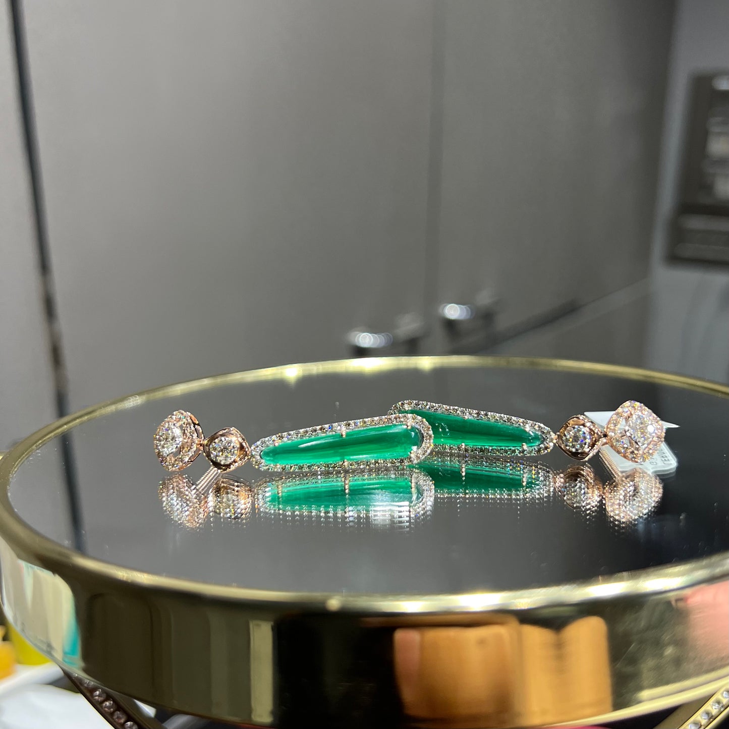 A pair of gold diamond earrings with green color stones set in a minimalist design.