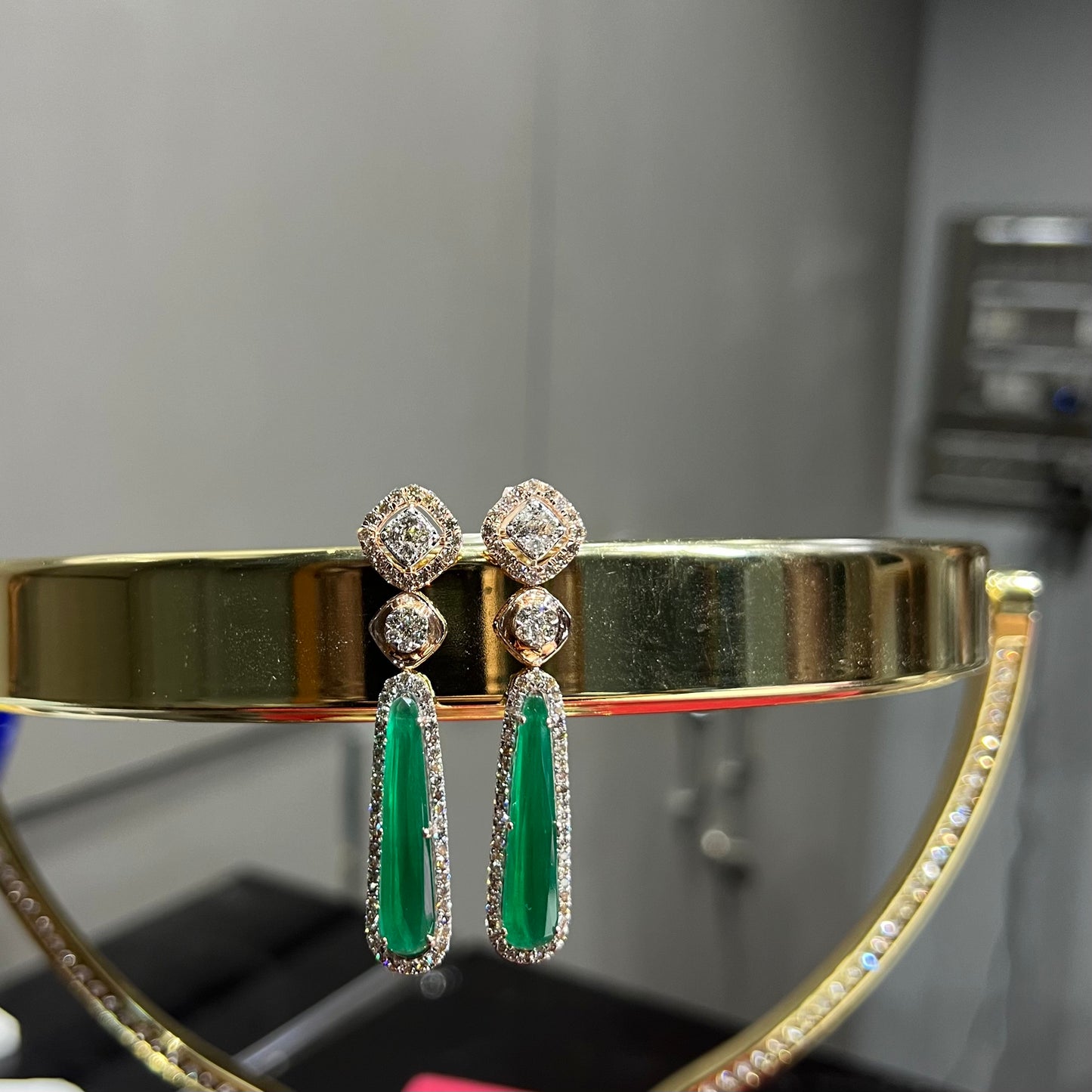 A pair of gold diamond earrings with green color stones set in a minimalist design.