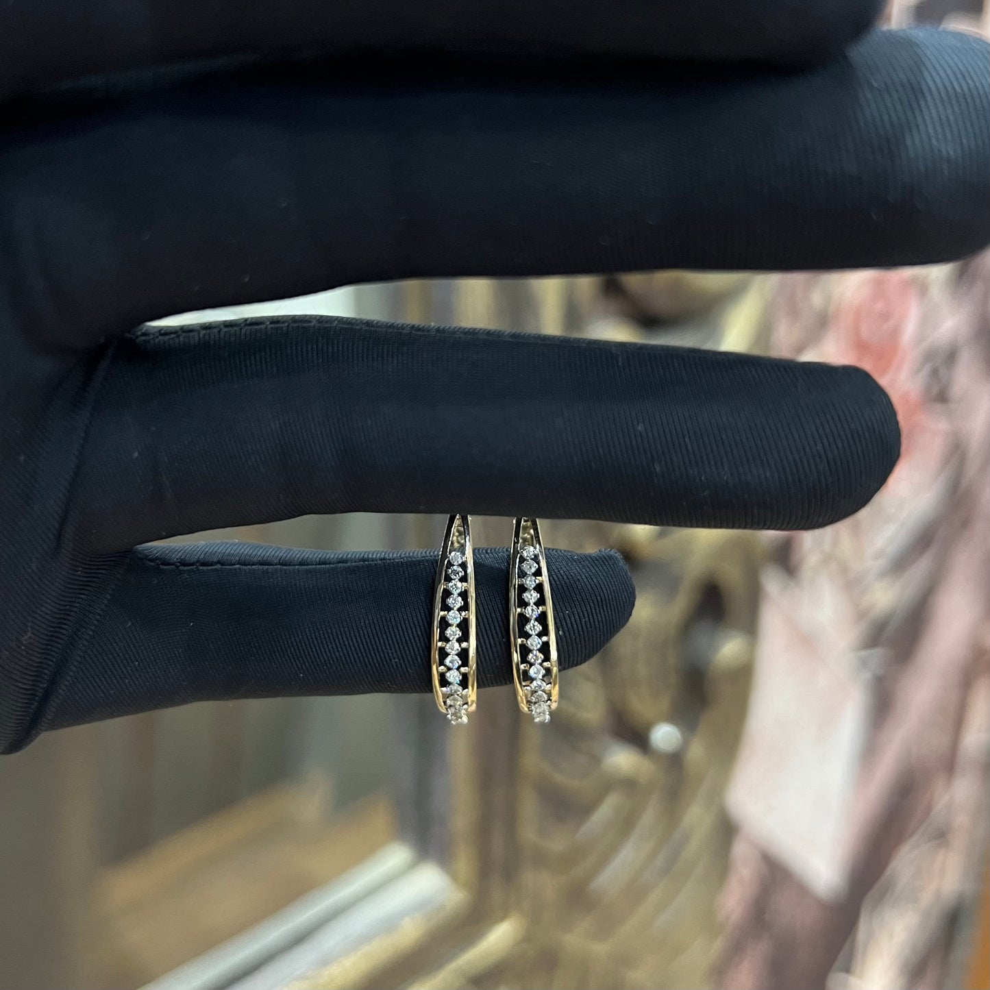 A pair of round-cut diamond earrings held in a person's hand, with a gold band.