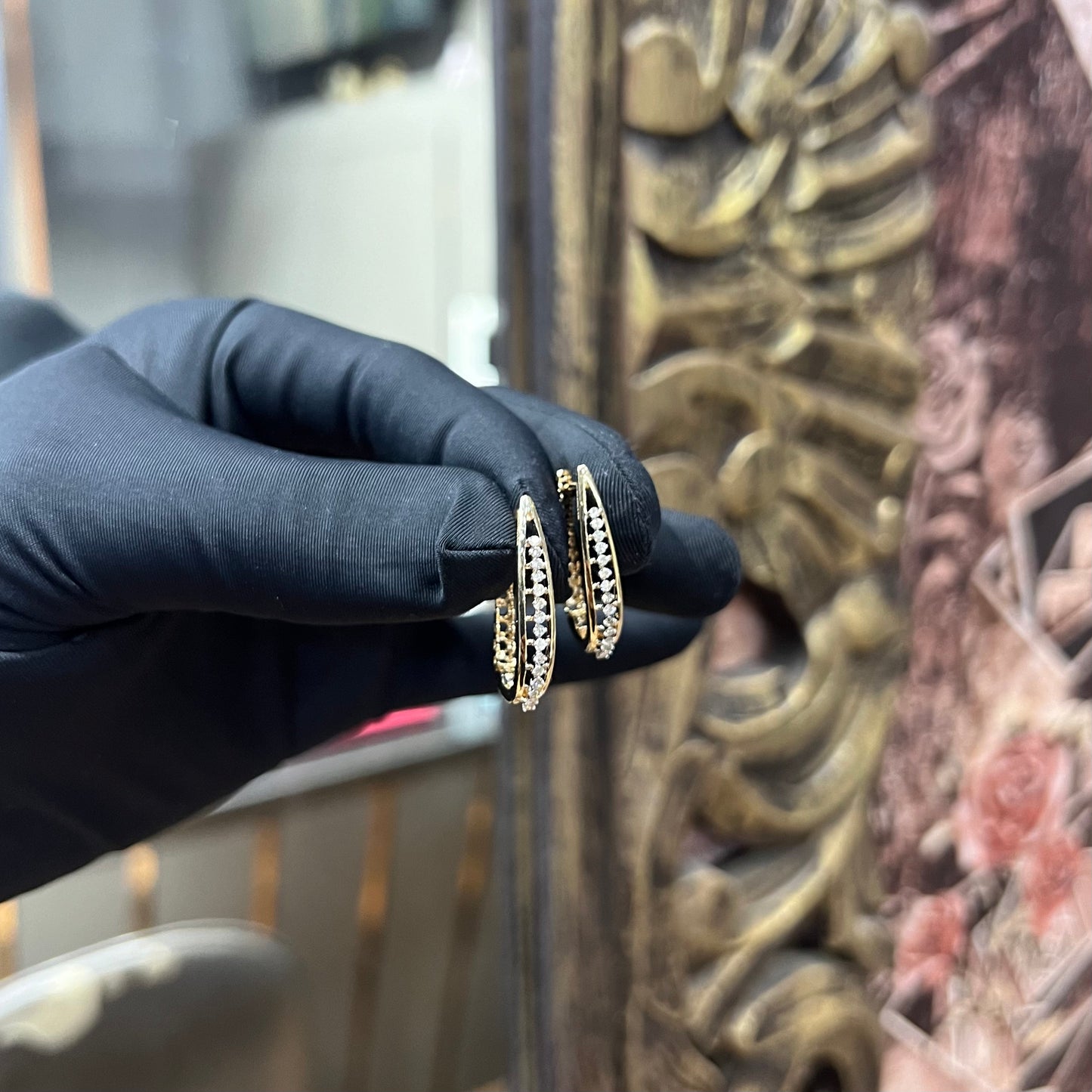 A pair of round-cut diamond earrings held in a person's hand, with a gold band.