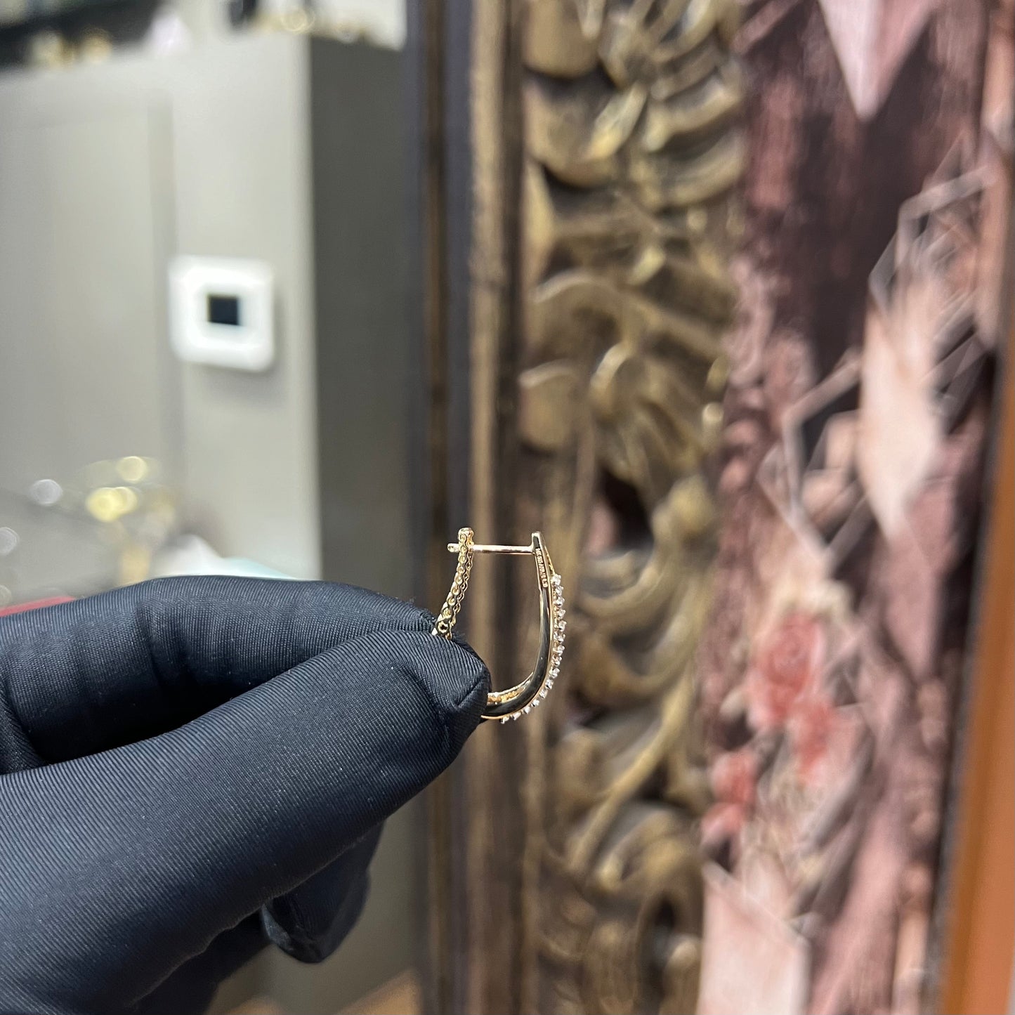 A pair of round-cut diamond hoop earrings held in a person's hand, with a gold band.