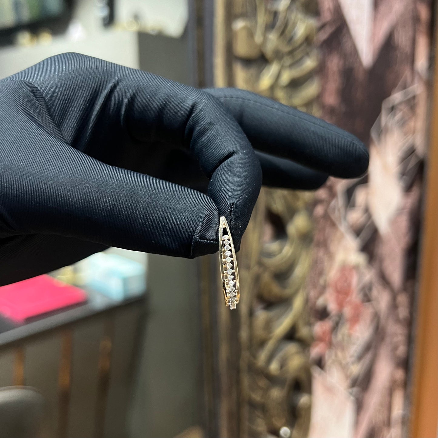 A pair of round-cut diamond hoop earrings held in a person's hand, with a gold band.