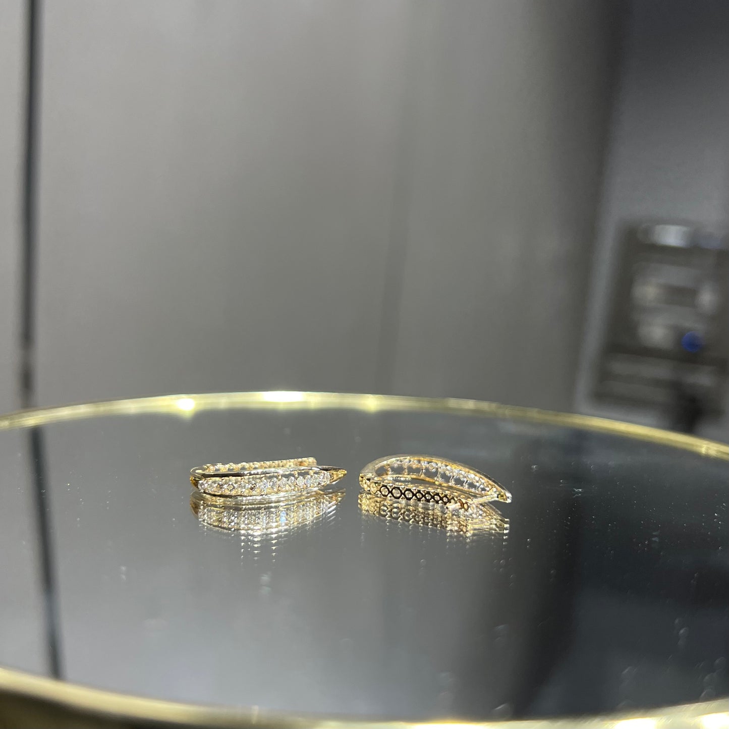 A pair of round-cut diamond hoop earrings held in a person's hand, with a gold band.