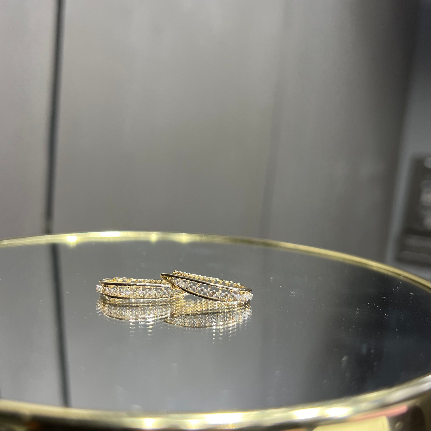 A pair of round-cut diamond hoop earrings held in a person's hand, with a gold band.