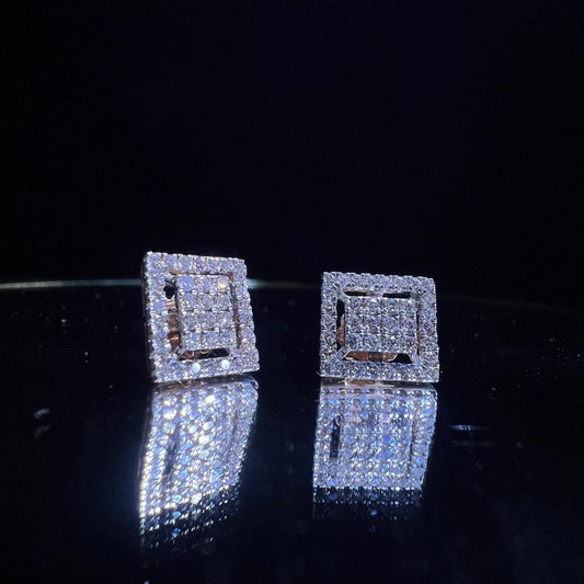 A pair of diamond stud earrings set in a gold casing, displayed against a reflective surface.