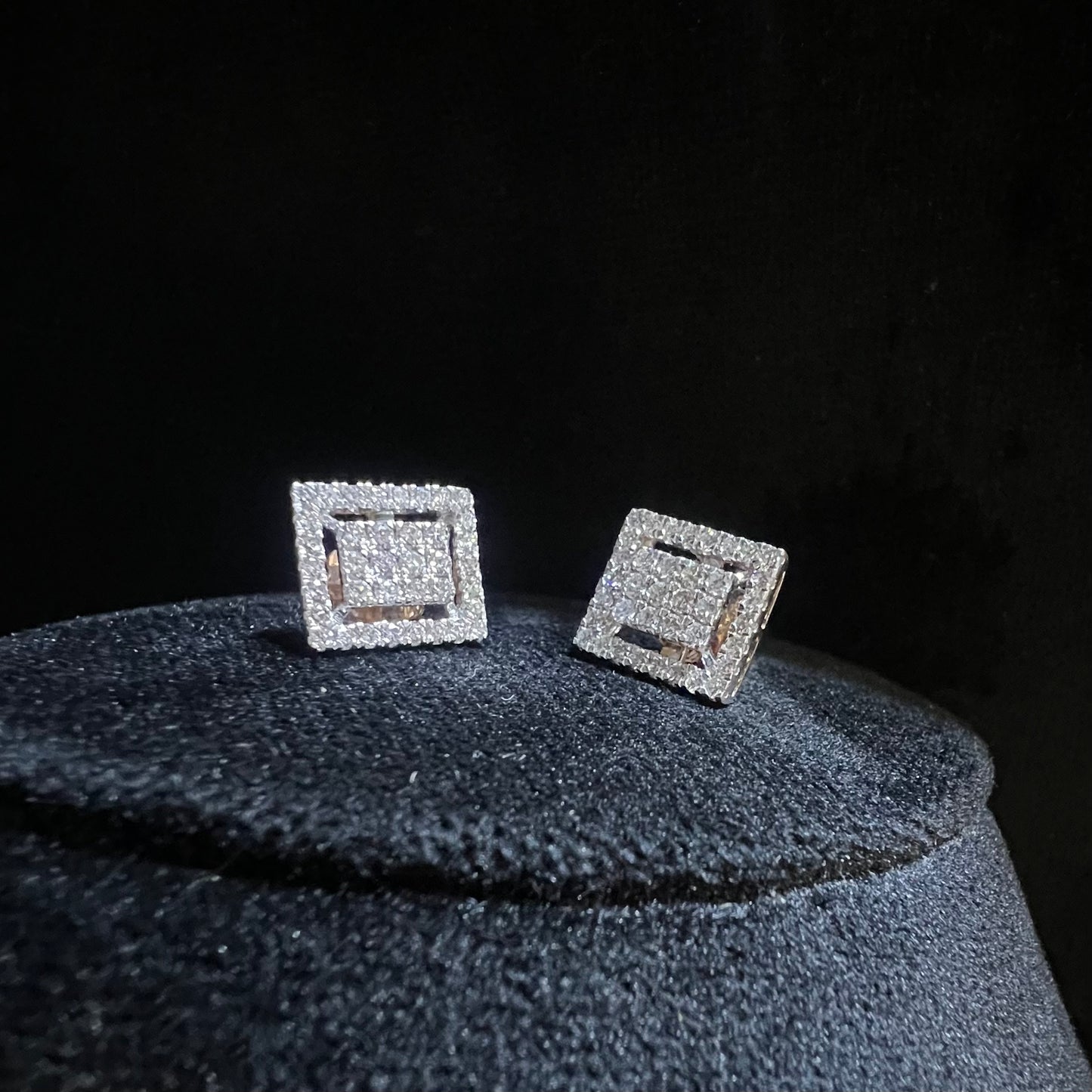 A pair of diamond stud earrings set in a gold casing, displayed against a reflective surface.
