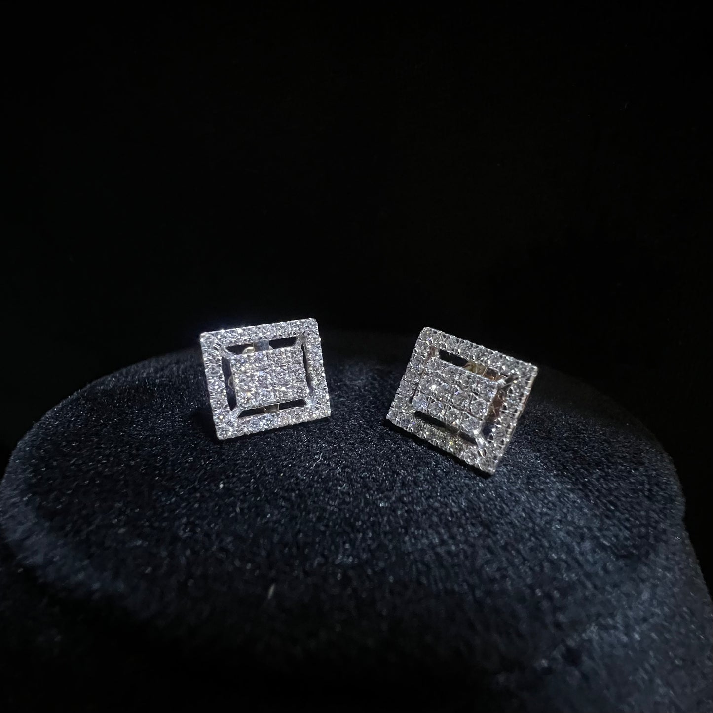 A pair of diamond stud earrings set in a gold casing, displayed against a mannequin stand.