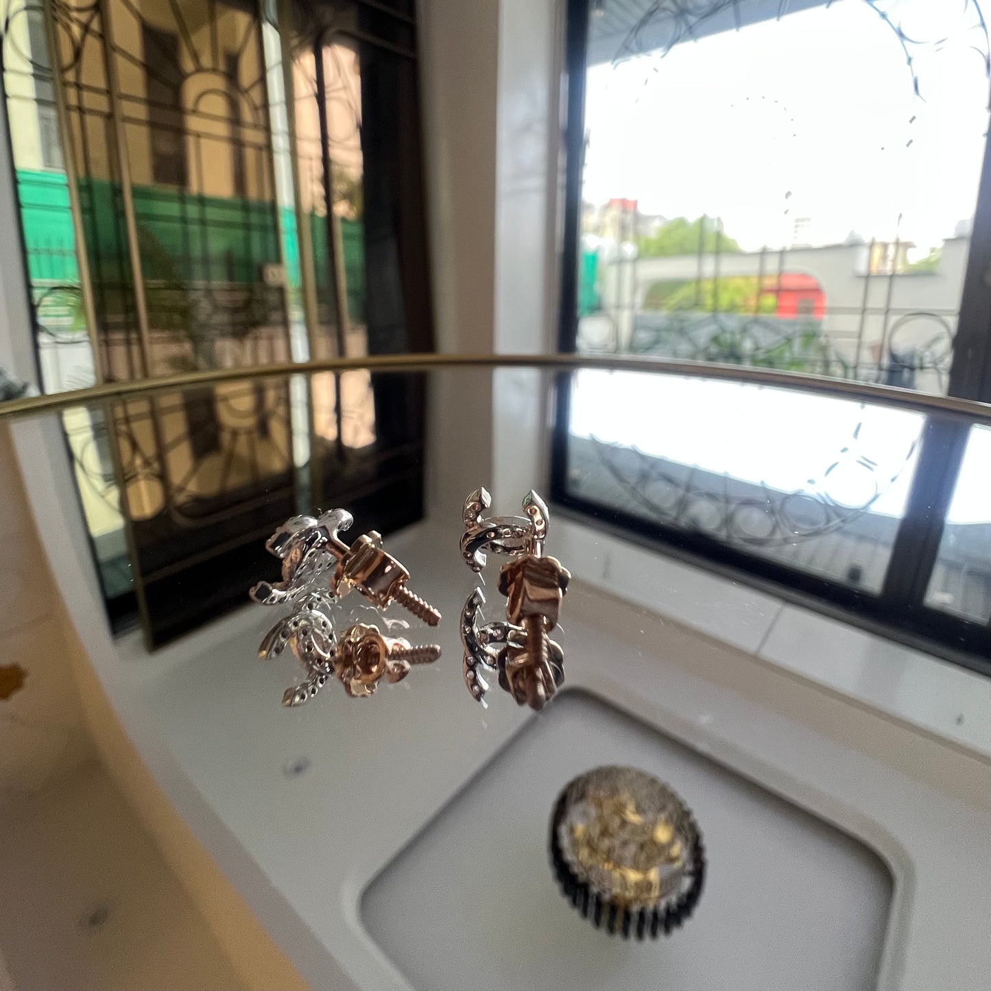 A pair of gold diamond earrings held on a reflective surface, with a clear and bright design.