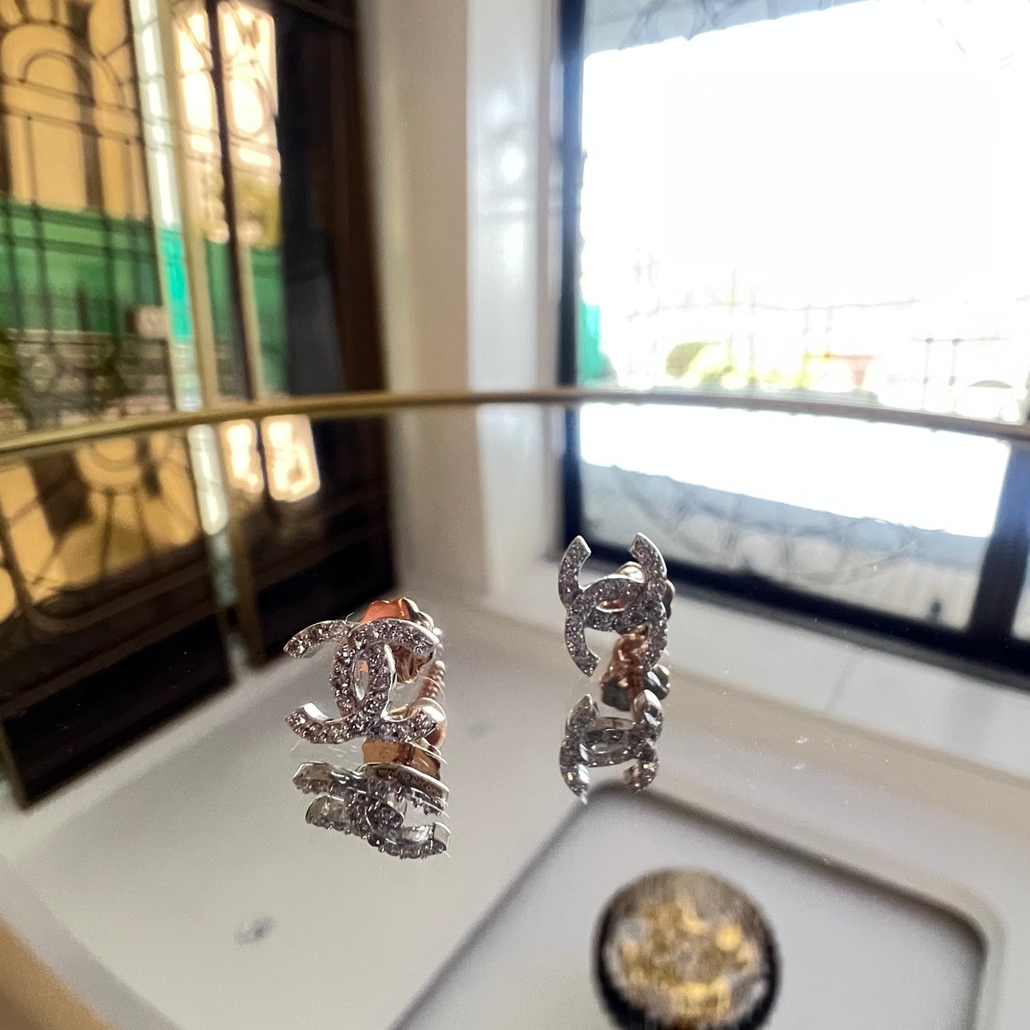 A pair of gold diamond earrings held on a reflective surface, with a clear and bright design.