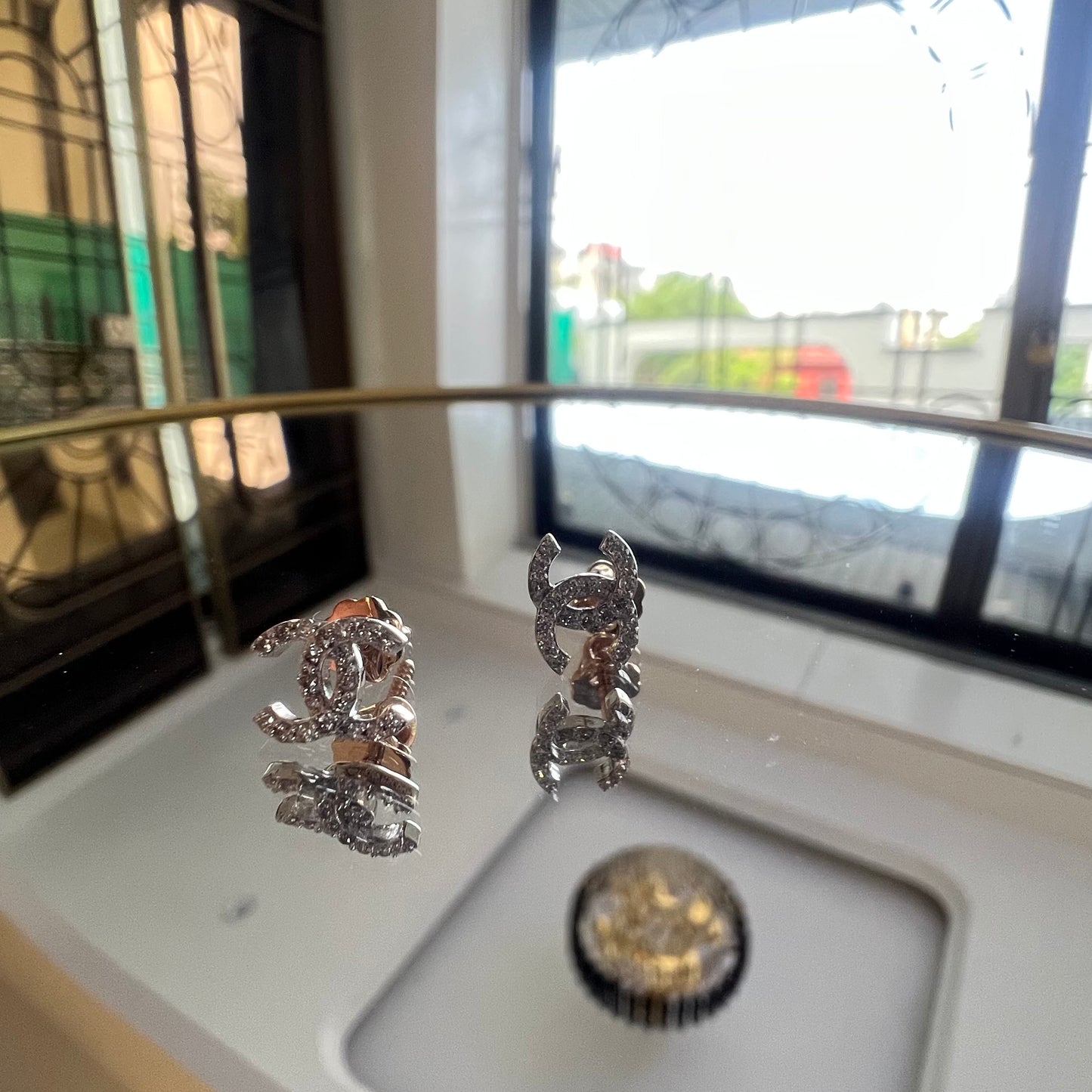 A pair of gold diamond earrings held on a reflective surface, with a clear and bright design.