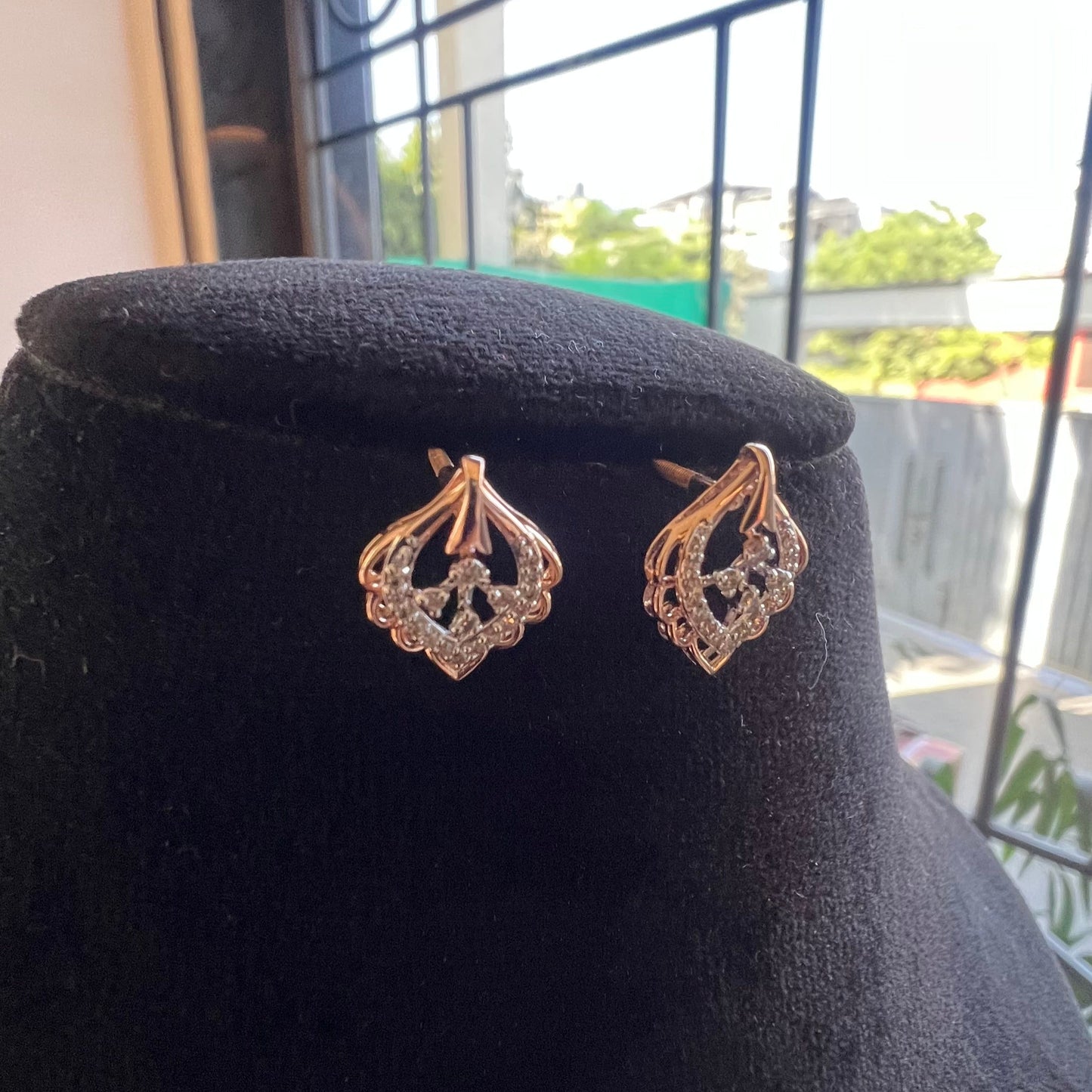 A pair of diamond stud earrings displayed on a black stand, with a mannequin jewelry stand in the background.