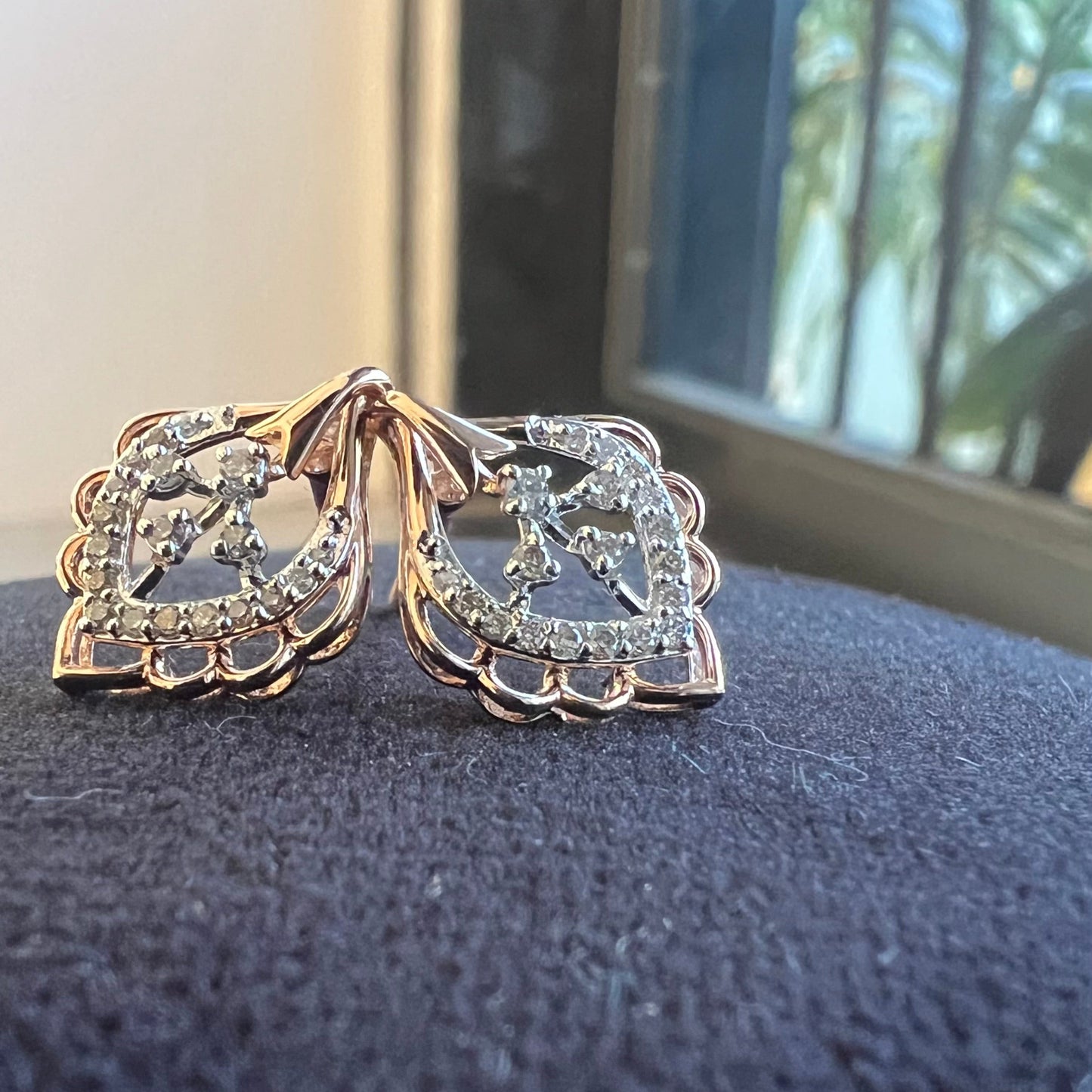 A pair of diamond stud earrings displayed on a black stand, with a mannequin jewelry stand in the background.
