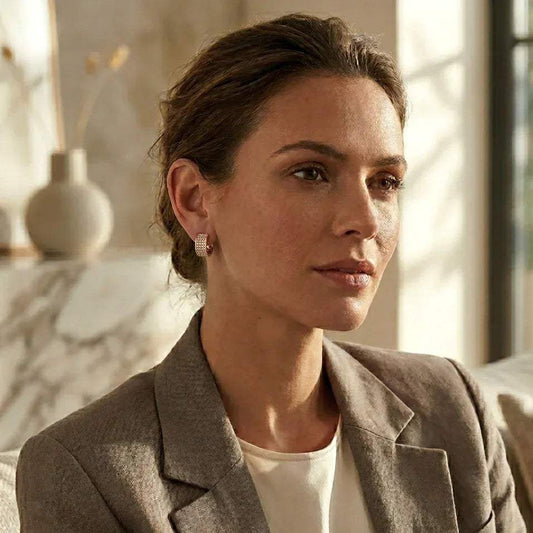 Woman wearing a beige blazer and diamond earrings in a softly lit room.