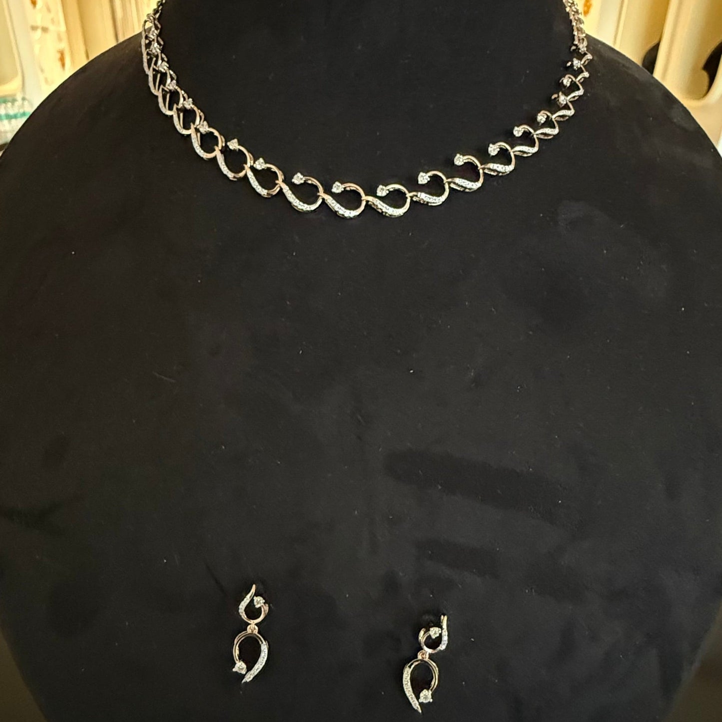 A gold diamond necklace with a chain link design, displayed on a mannequin bust, accompanied by a pair of matching earrings with a geometric design.