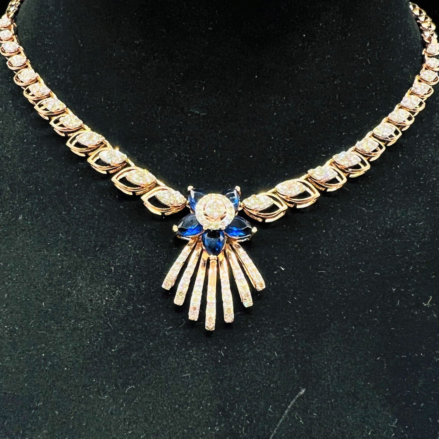 A gold wedding necklace with round-cut blue color stones and clear diamonds displayed on a mannequin bust.