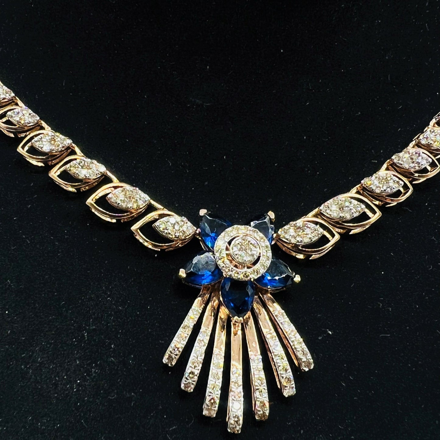 A gold wedding necklace with round-cut blue color stones and clear diamonds displayed on a mannequin bust.