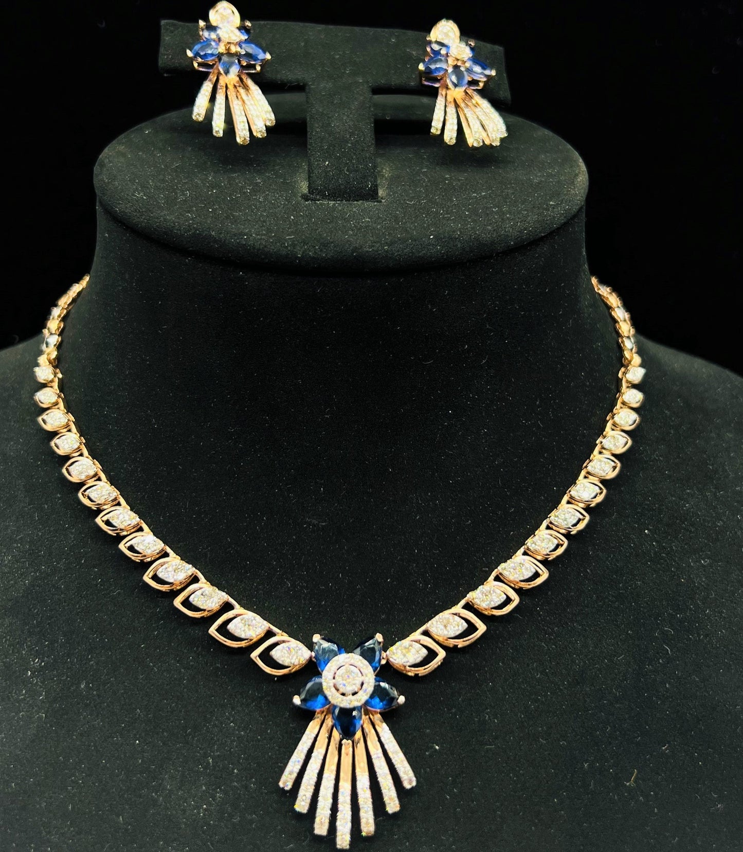 A gold wedding necklace with round-cut blue color stones and clear diamonds with matching earrings displayed on a mannequin bust.