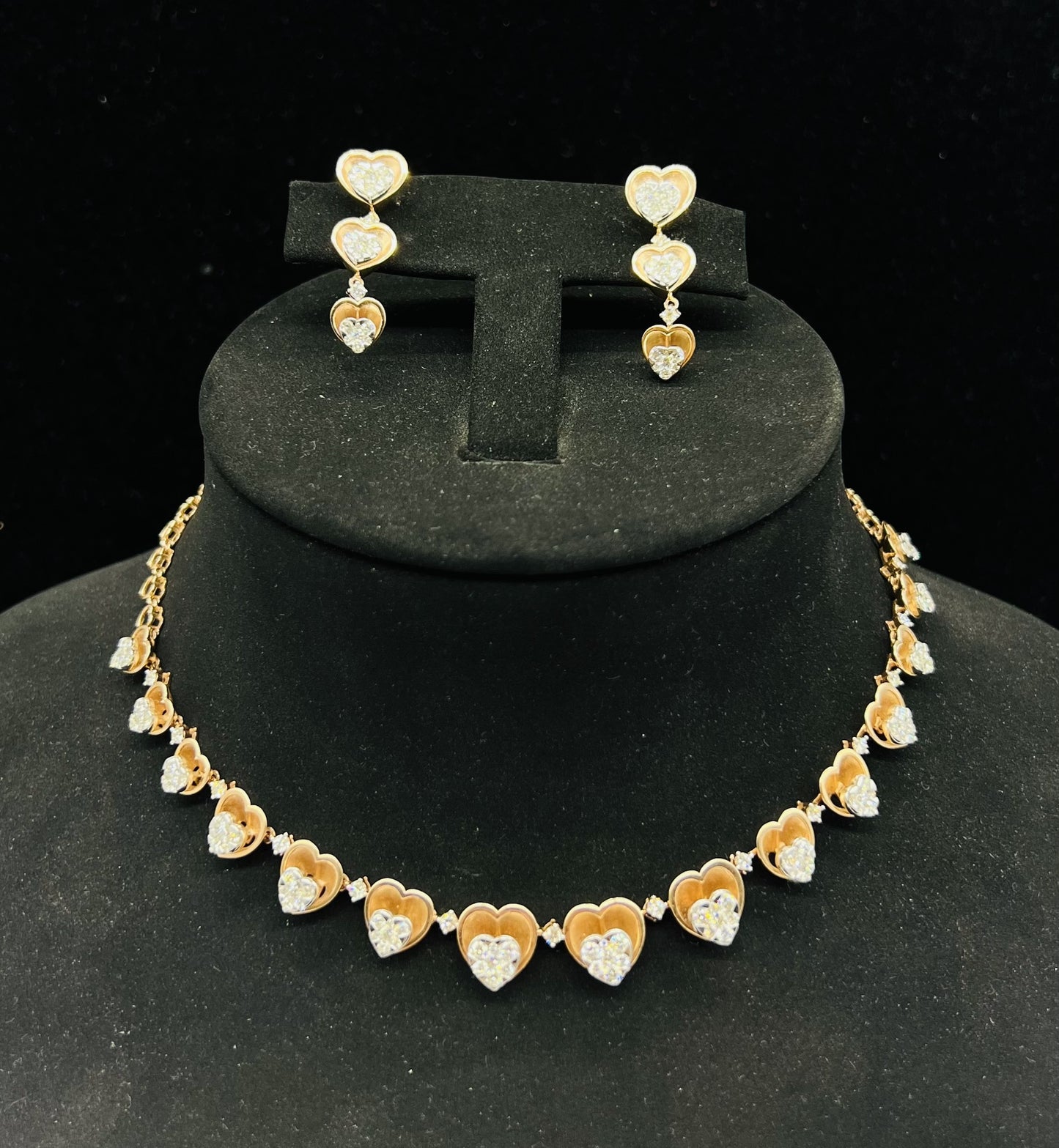 A gold necklace with round-cut diamond pendants and coordinating earrings, displayed on a black mannequin bust.