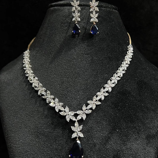 Diamond necklace set with color stone drop pendant and matching floral diamond earrings displayed on black stand.