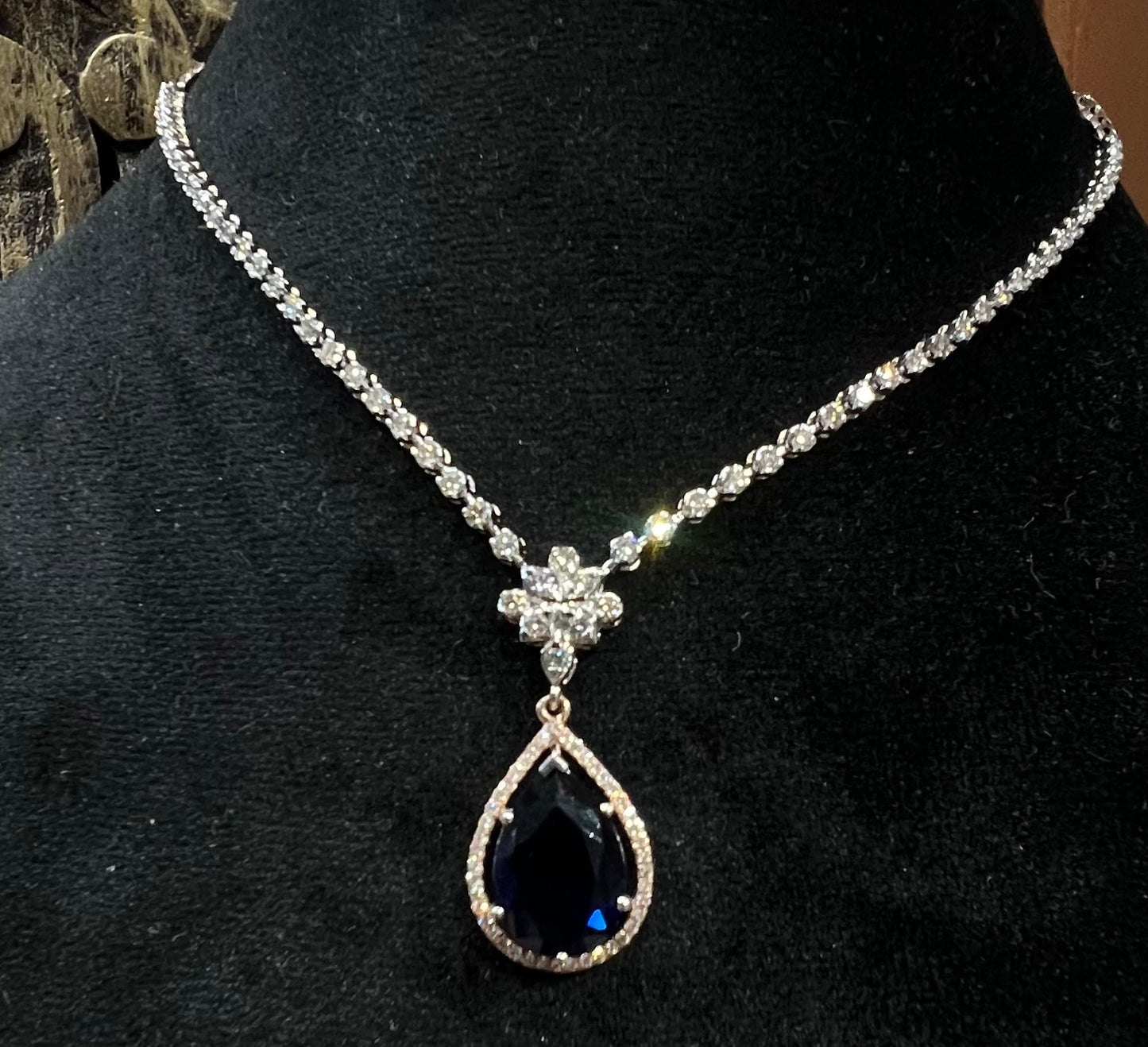 Elegant diamond necklace set with teardrop color stone pendant on black display