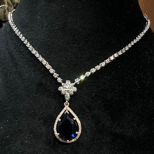 Elegant diamond necklace set with teardrop color stone pendant on black display