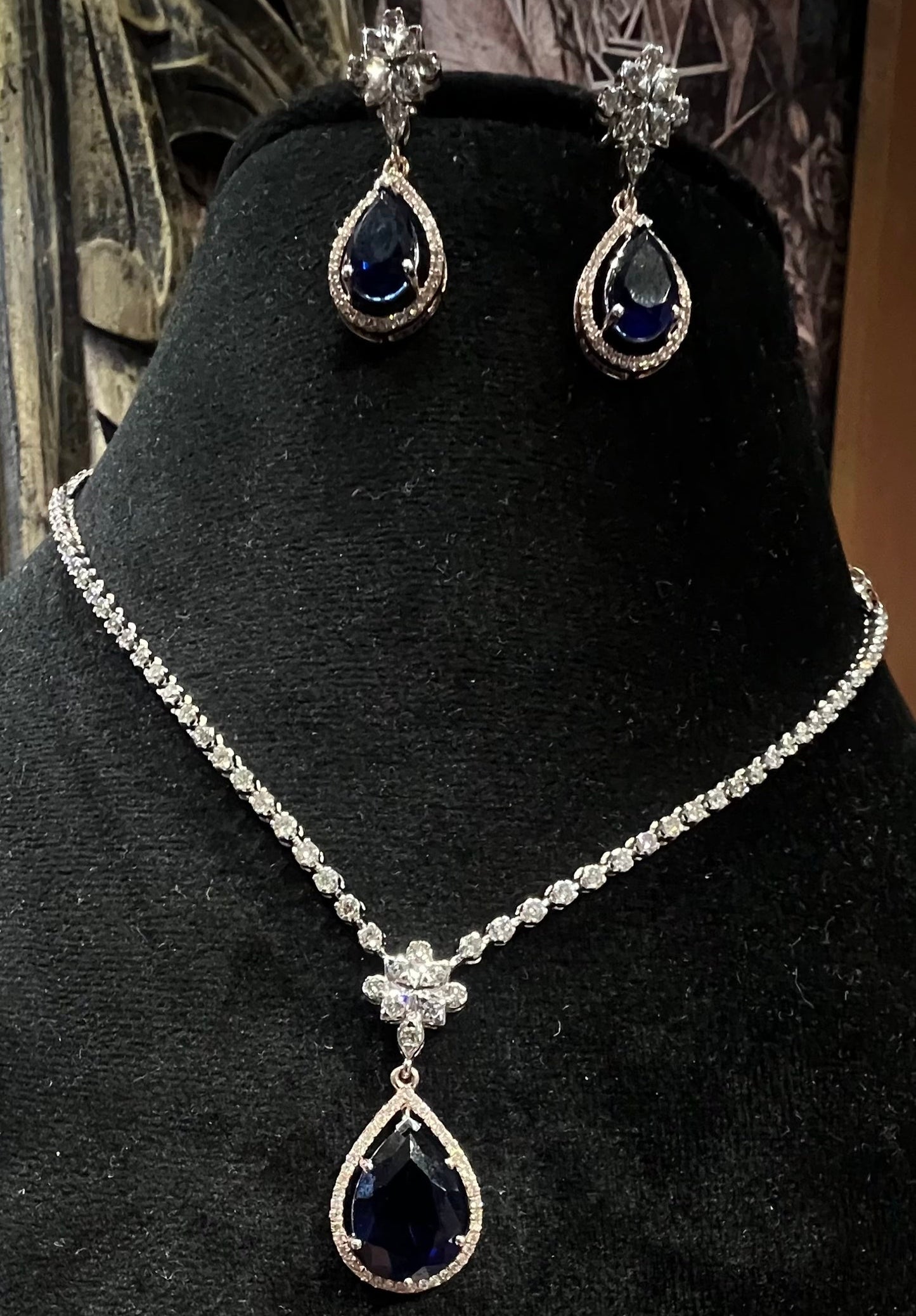 Elegant diamond necklace set with teardrop color stone pendant and matching earrings on black display