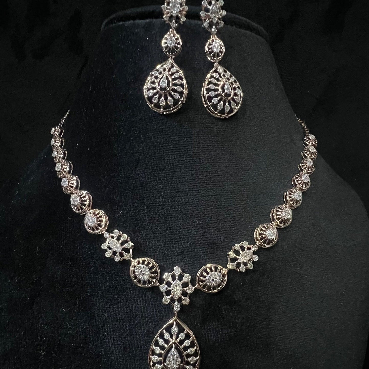 Elegant teardrop-shaped diamond necklace set with floral-inspired motifs and matching earrings displayed on a black background.