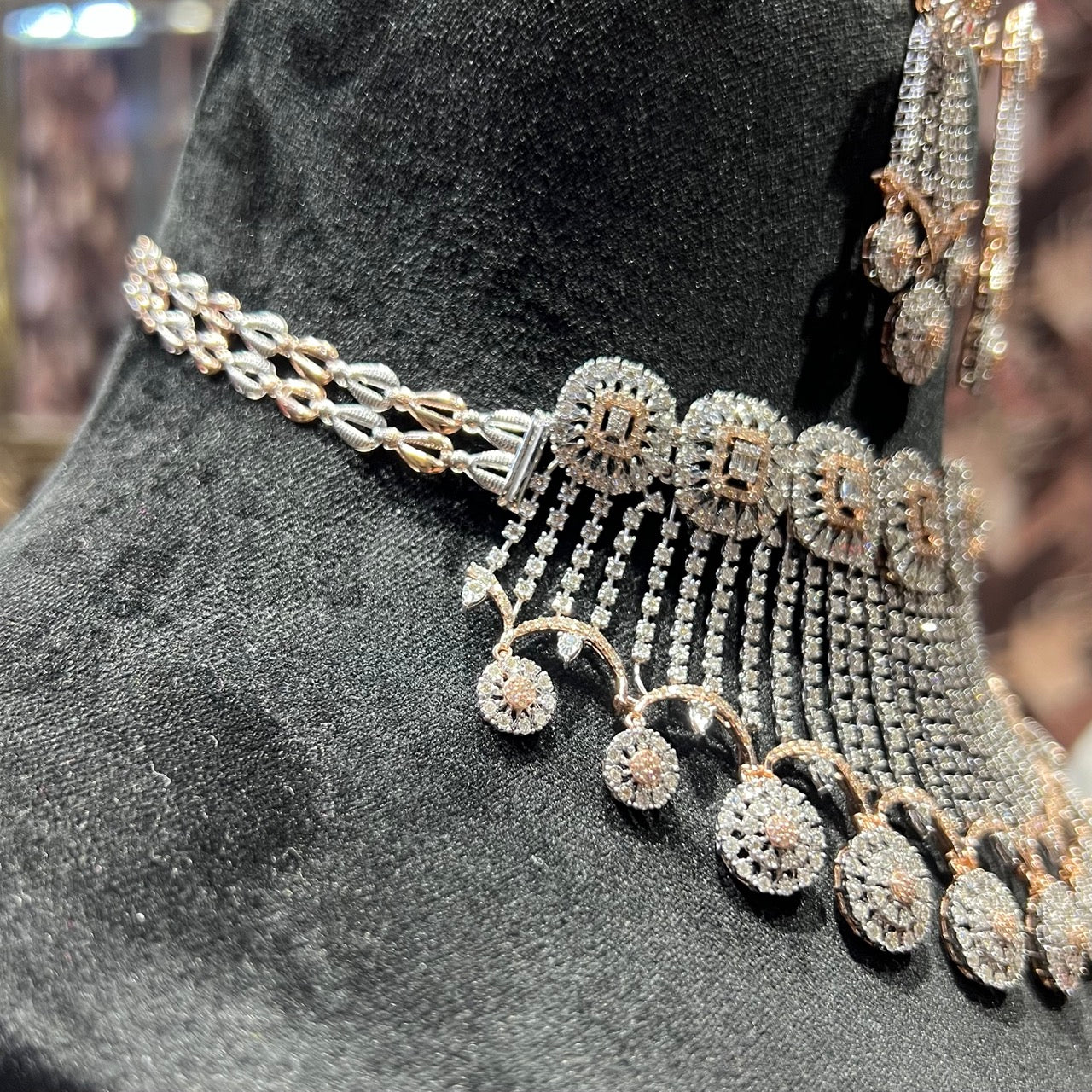 Close-up of a luxurious diamond necklace set with matching earrings featuring circular motifs and cascading diamond strands on a black display stand.