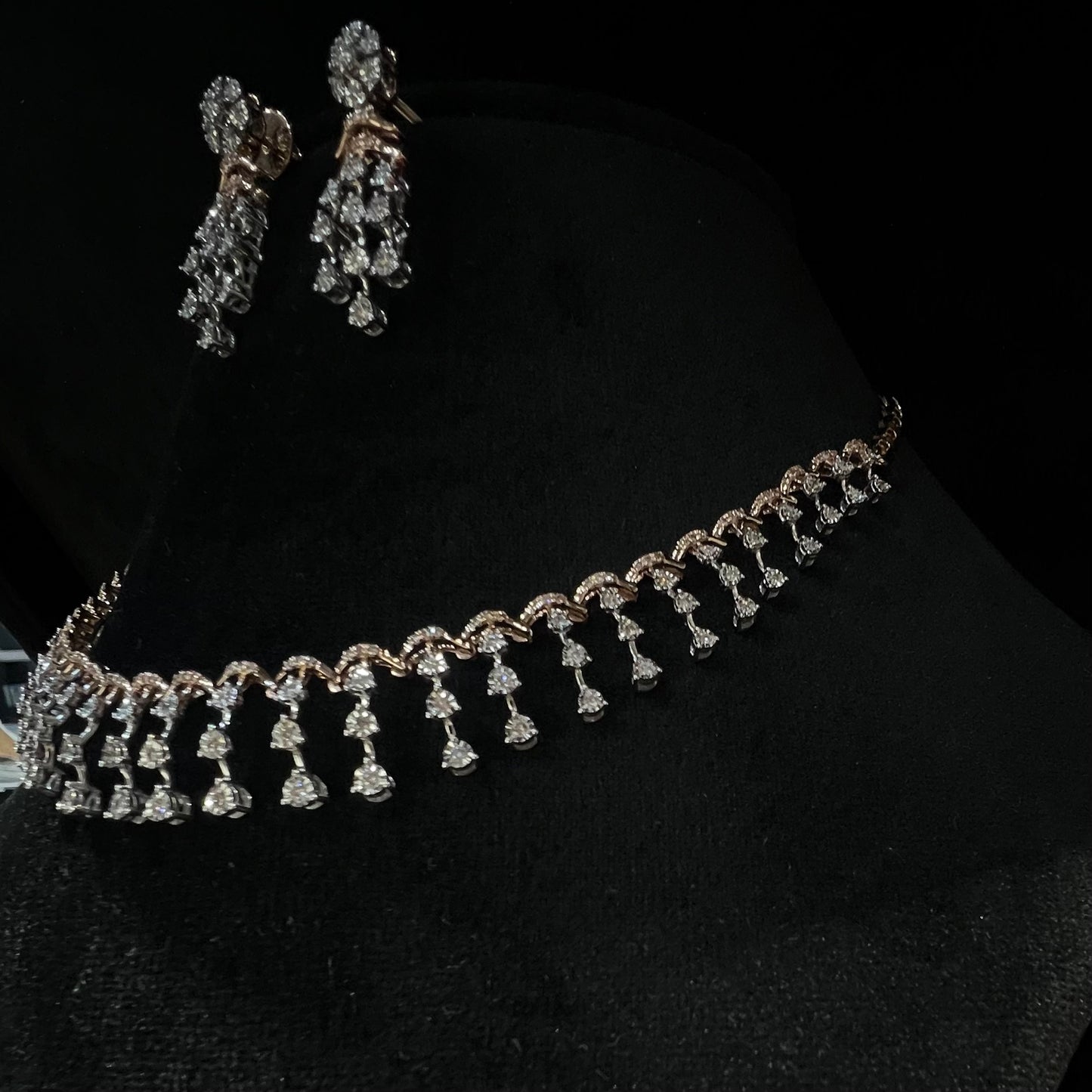 A gold diamond necklace with a series of round and marquise shaped earrings attached to the neckline, set on a black mannequin.