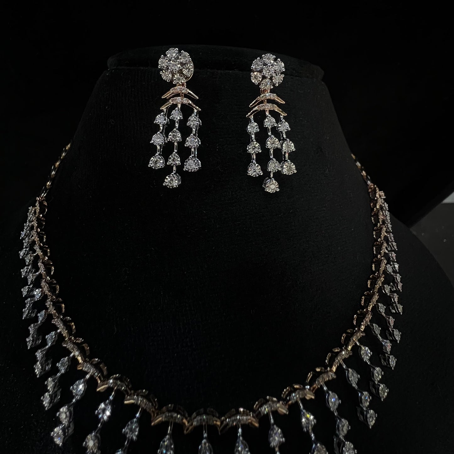 A gold diamond necklace with a series of round and marquise shaped earrings attached to the neckline, set on a black mannequin.