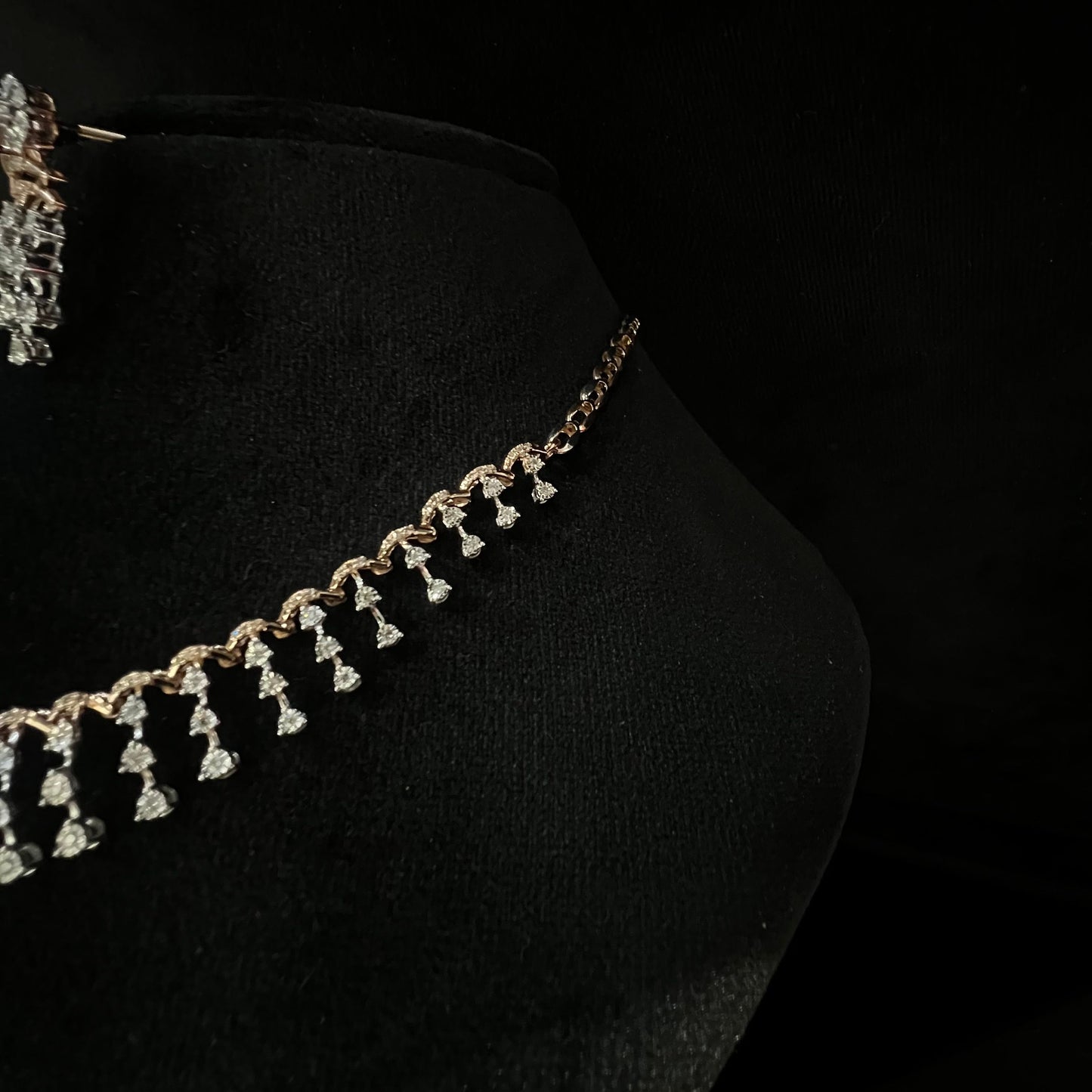 A gold diamond necklace with a series of round and marquise shaped earrings attached to the neckline, set on a black mannequin.