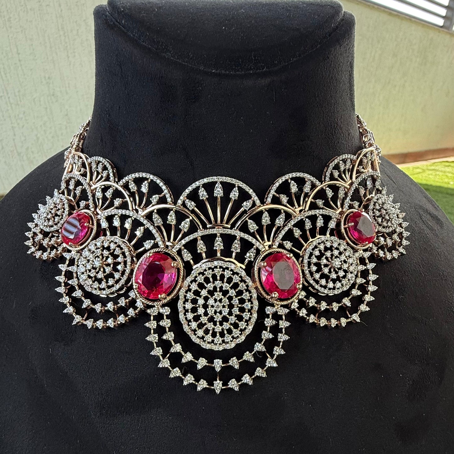 A gold diamond choker necklace with a floral pattern and red and white diamonds, displayed on a mannequin.