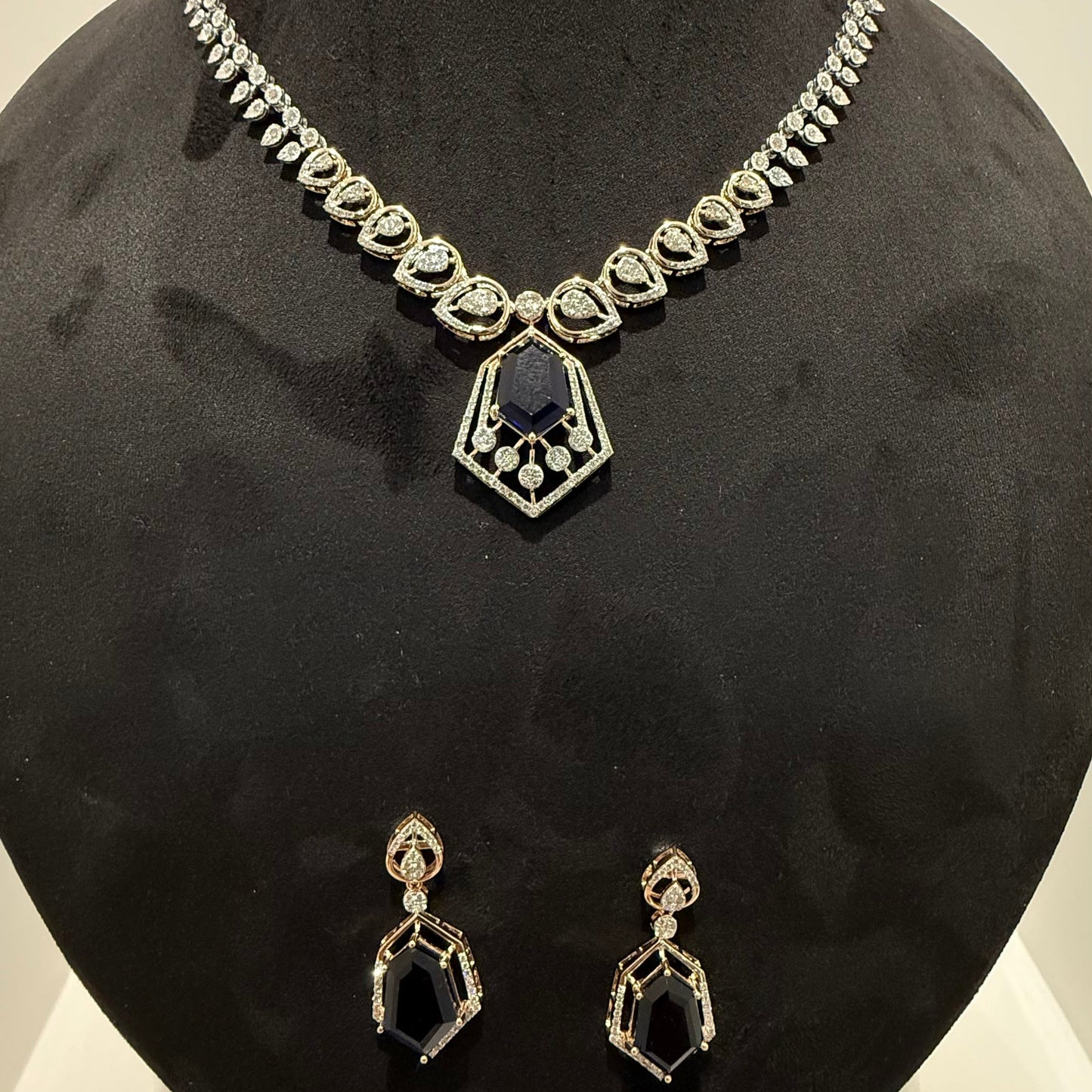 A gold diamond necklace with a geometric pendant and matching earrings displayed on a mannequin bust.