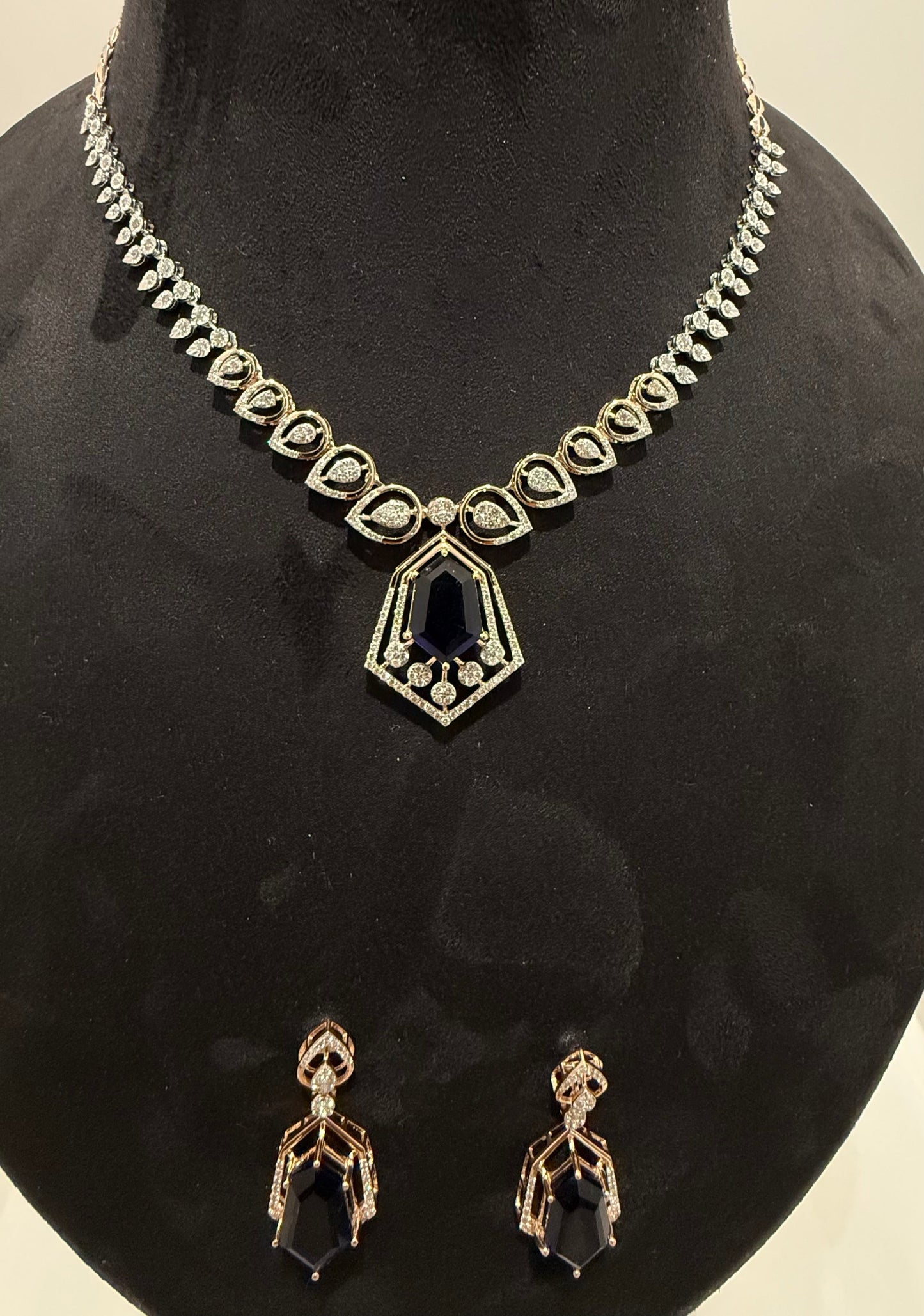 A gold diamond necklace with a geometric pendant and matching earrings displayed on a mannequin bust.
