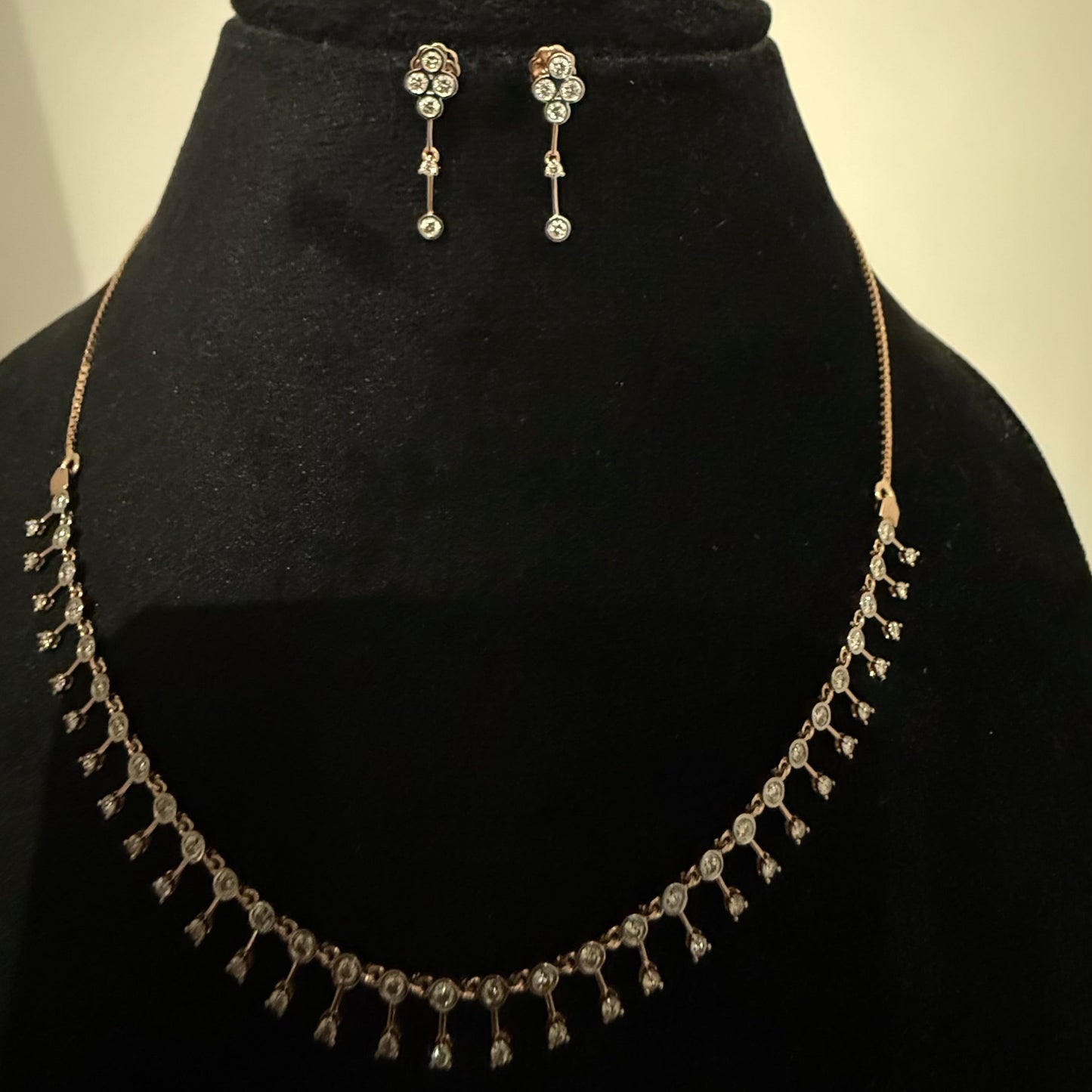 A mannequin showcasing a minimalist diamond necklace and earrings set in gold.