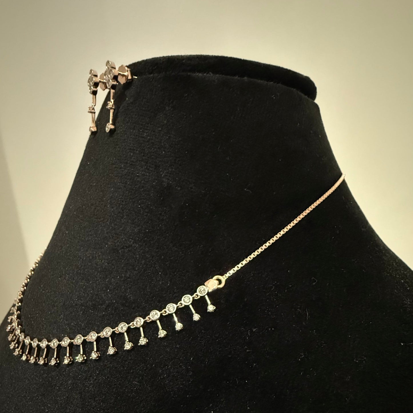 A mannequin showcasing a minimalist diamond necklace and earrings set in gold.