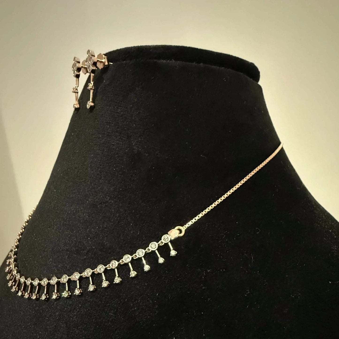 A mannequin showcasing a minimalist diamond necklace and earrings set in gold.