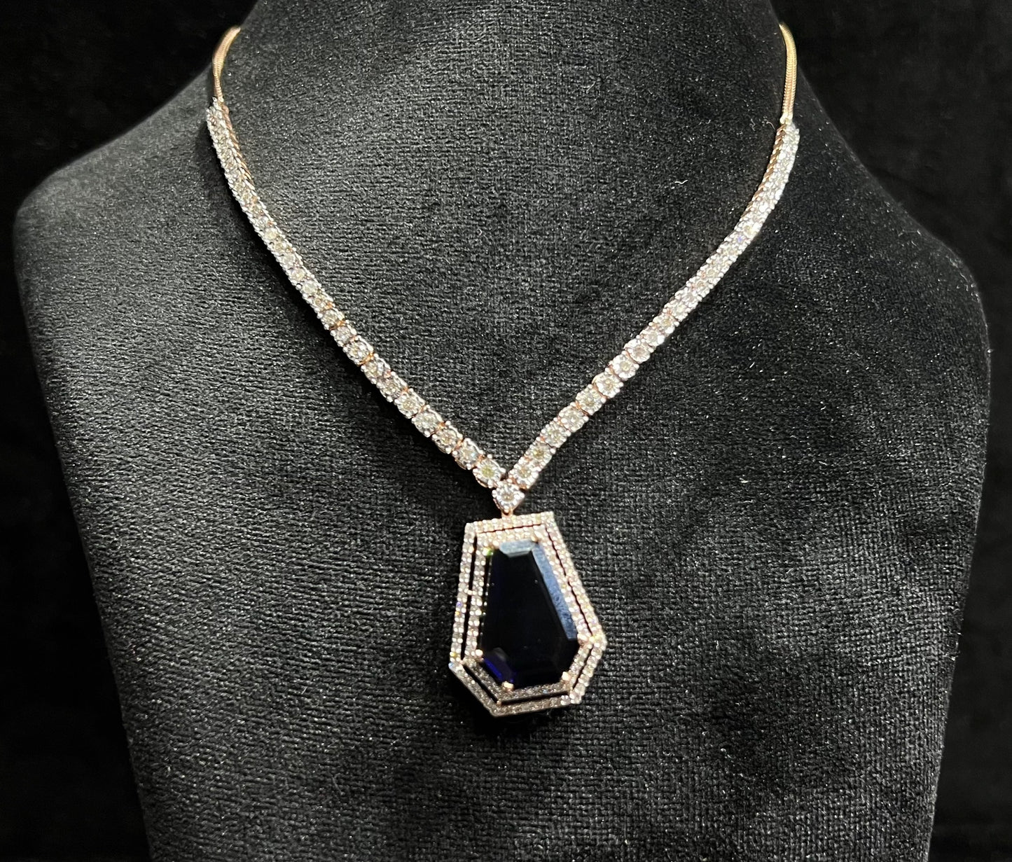 A diamond necklace set featuring a striking geometric deep blue gemstone pendant, all displayed on a black velvet background.
