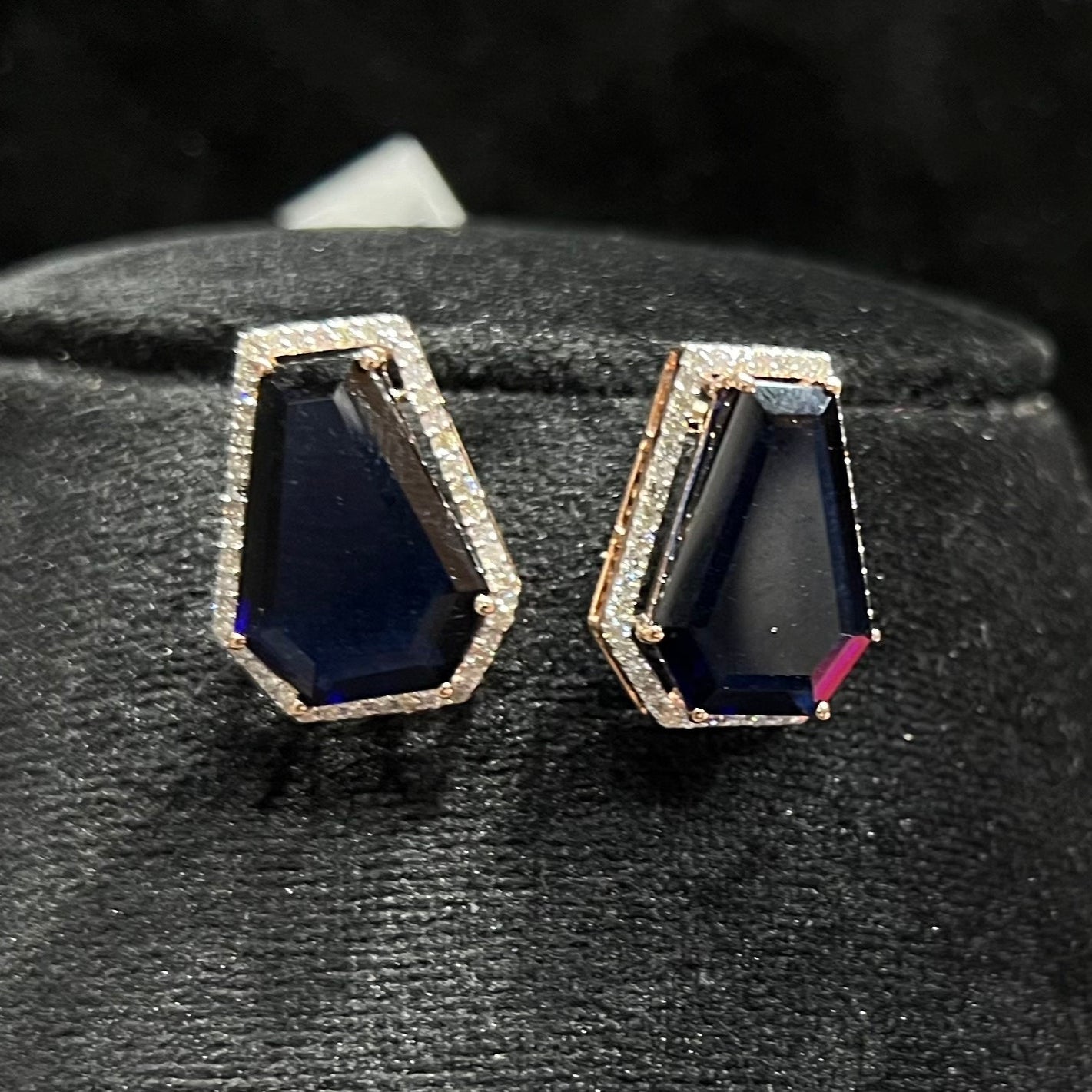 A diamond earrings set featuring a striking geometric deep blue gemstone, all displayed on a black velvet background.