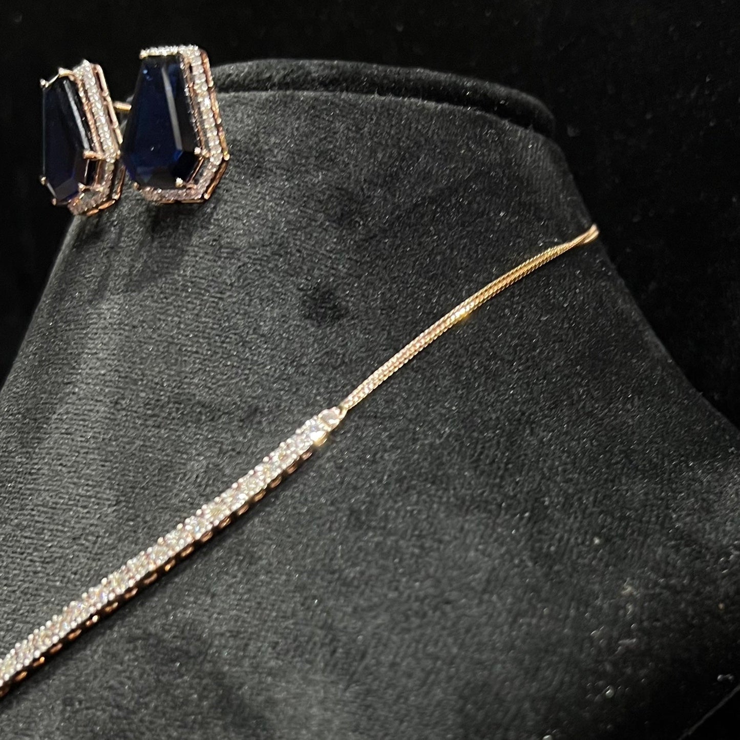 A diamond necklace set featuring a striking geometric deep blue gemstone with matching earrings, all displayed on a black velvet background from left side.