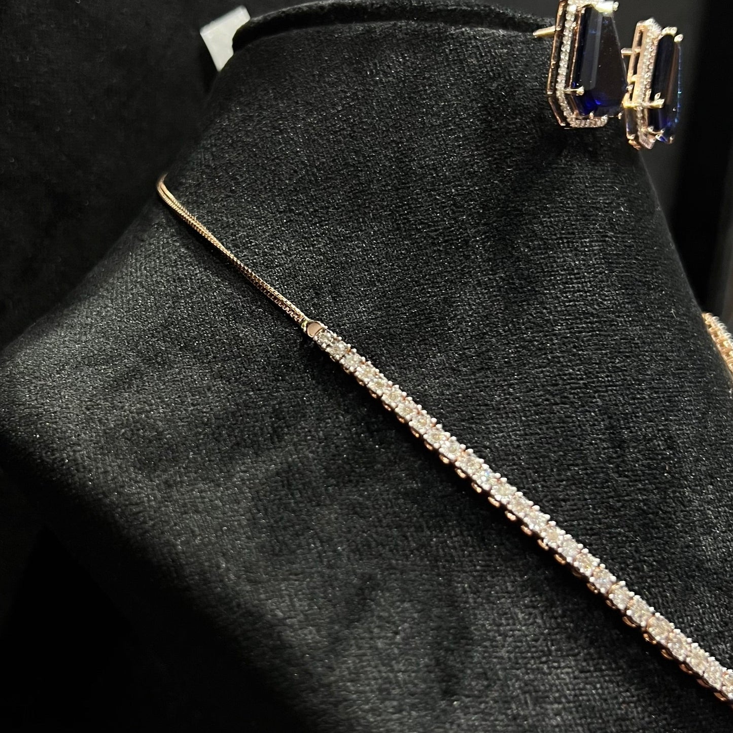 A diamond necklace set featuring a striking geometric deep blue gemstone with matching earrings, all displayed on a black velvet background from left side.