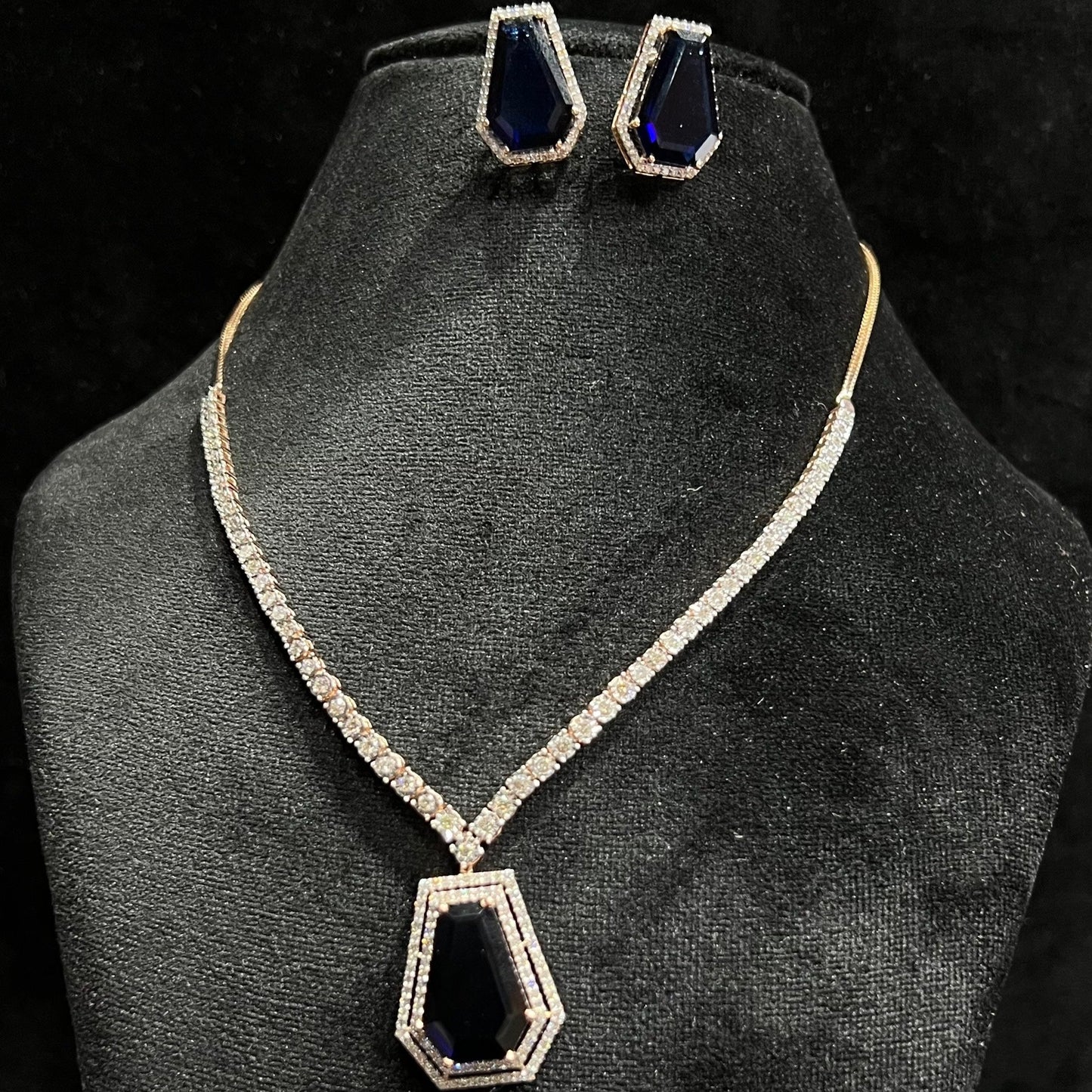 A diamond necklace set featuring a striking geometric deep blue gemstone pendant with matching earrings, all displayed on a black velvet background.