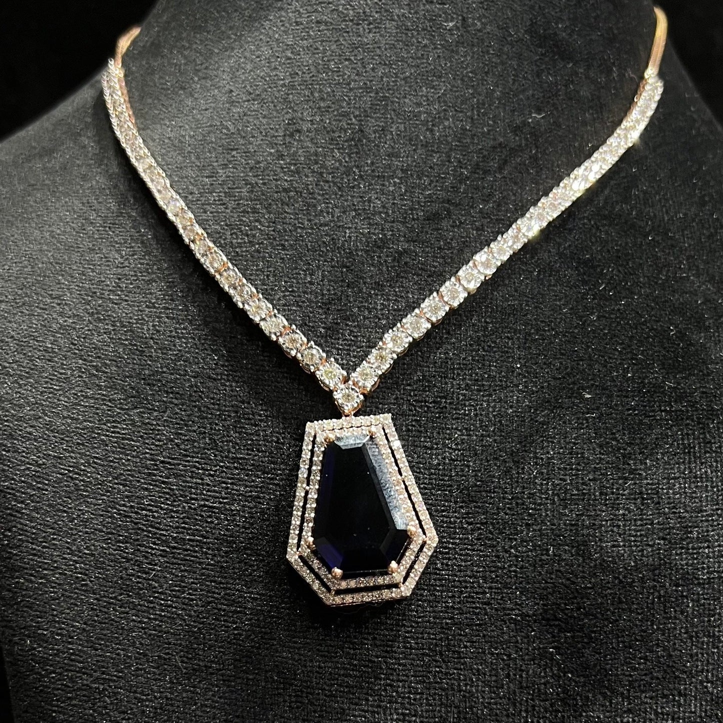 A diamond necklace set featuring a striking geometric deep blue gemstone pendant, all displayed on a black velvet background.