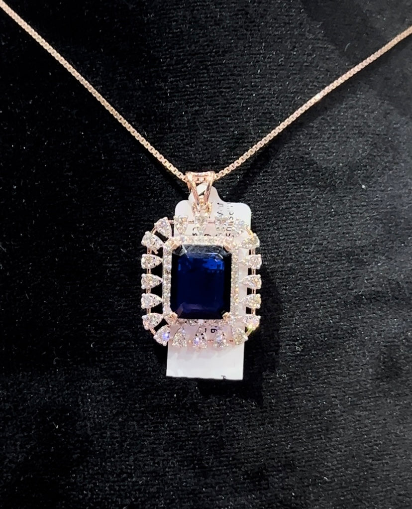A gold diamond pendant with a blue center stone surrounded by smaller white diamonds, attached to a gold chain for earrings.