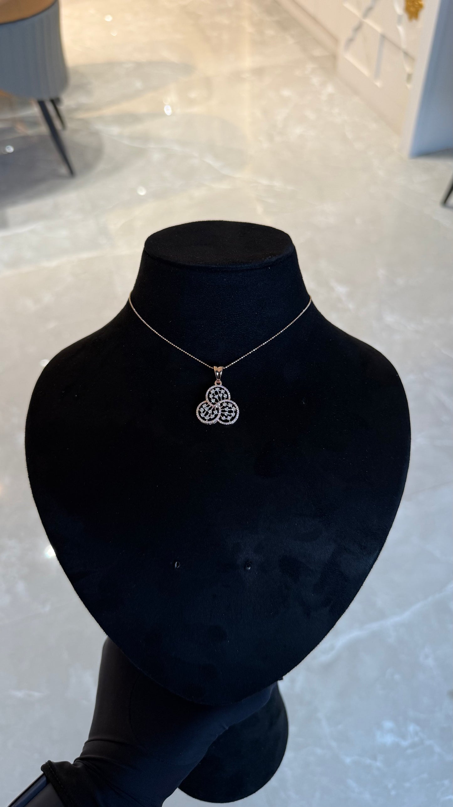 A gold diamond pendant with a floral design, displayed on a black mannequin necklace stand.