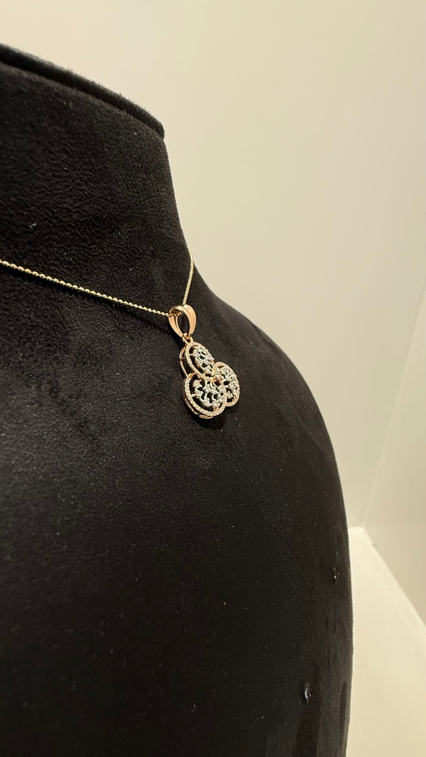 A gold diamond pendant with a floral design, displayed on a black mannequin necklace stand.