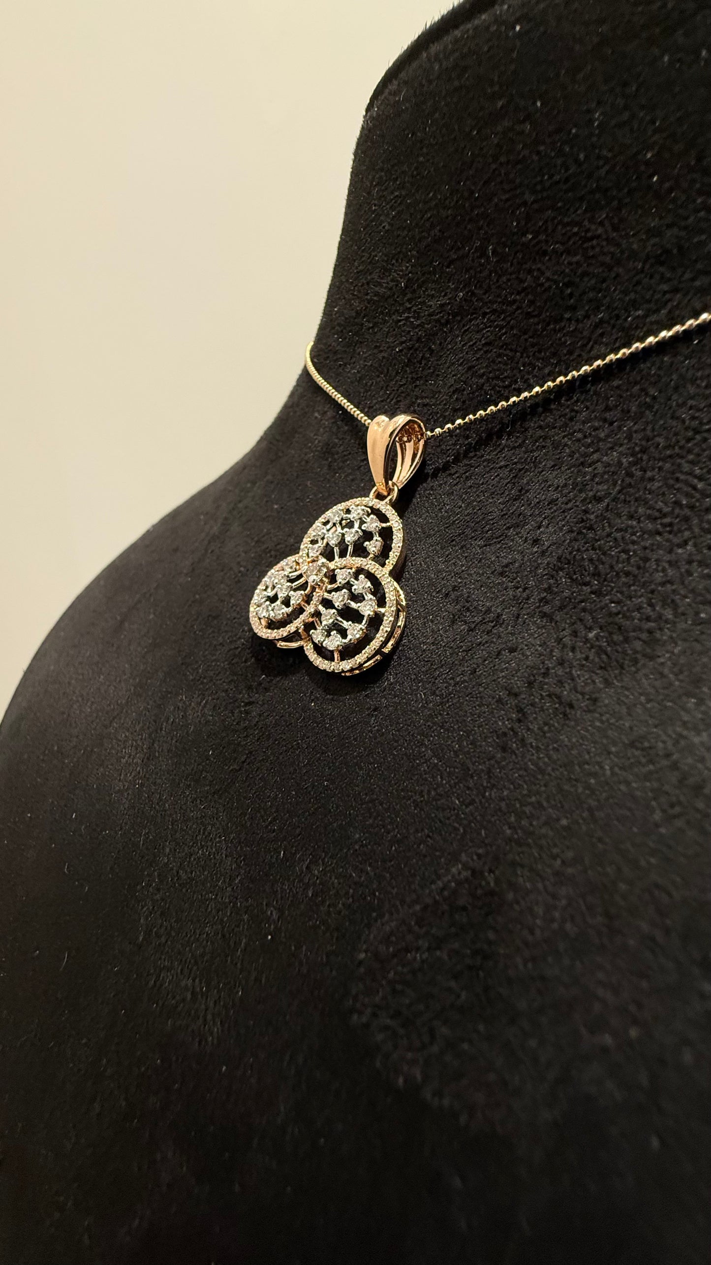 A gold diamond pendant with a floral design, displayed on a black mannequin necklace stand.