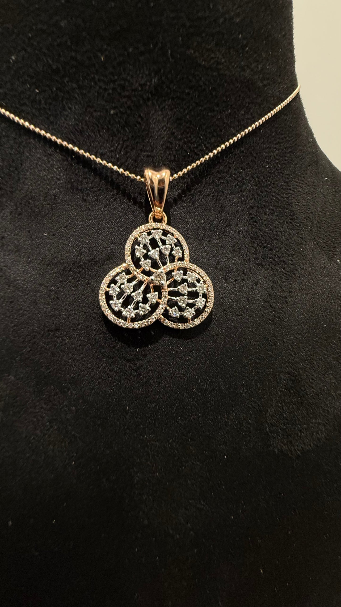 A gold diamond pendant with a floral design, displayed on a black mannequin necklace stand.