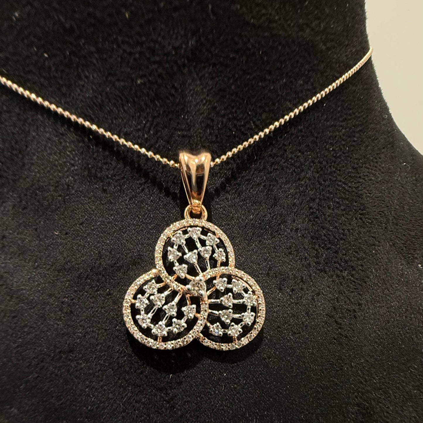 A gold diamond pendant with a floral design, displayed on a black mannequin necklace stand.