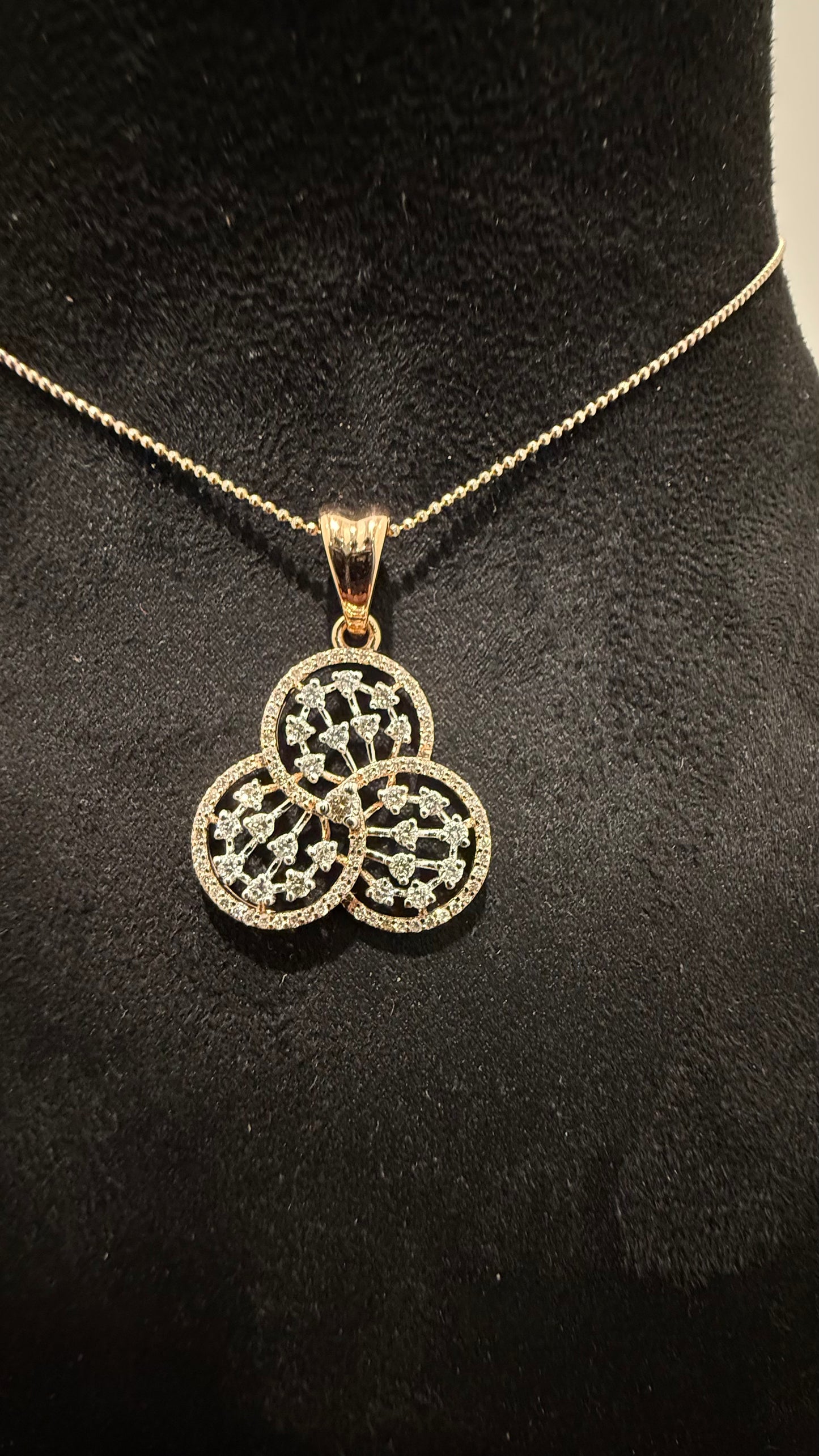 A gold diamond pendant with a floral design, displayed on a black mannequin necklace stand.